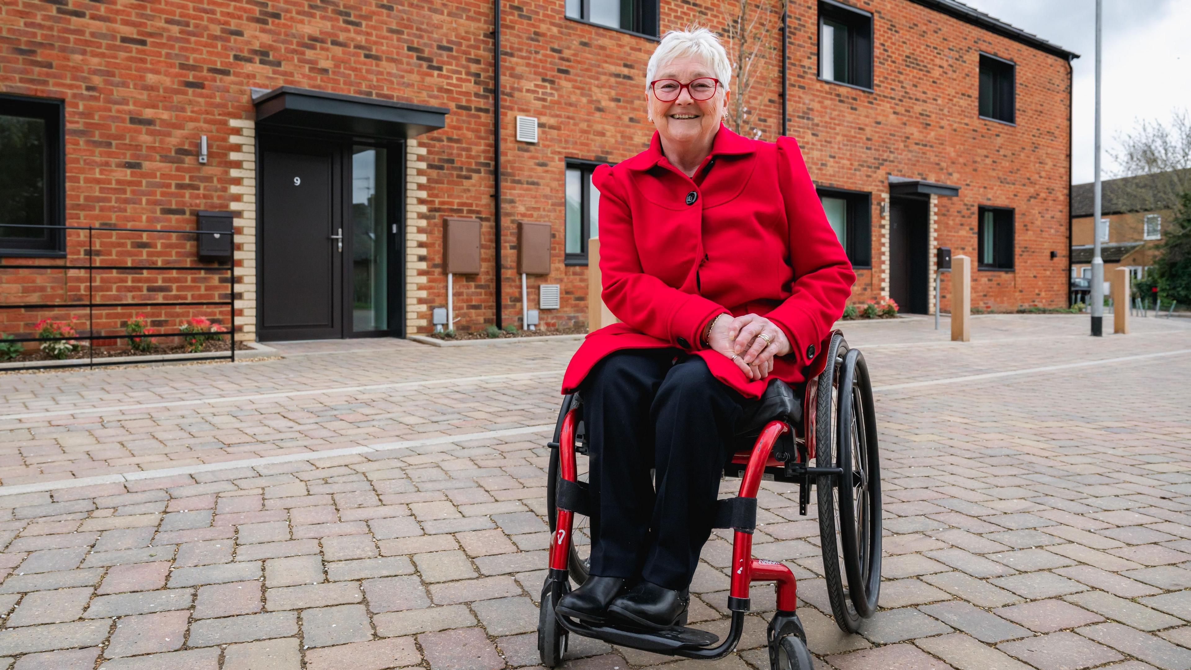 Gerri Bird, a wheelchair user, is smiling against a backdrop of new-build houses