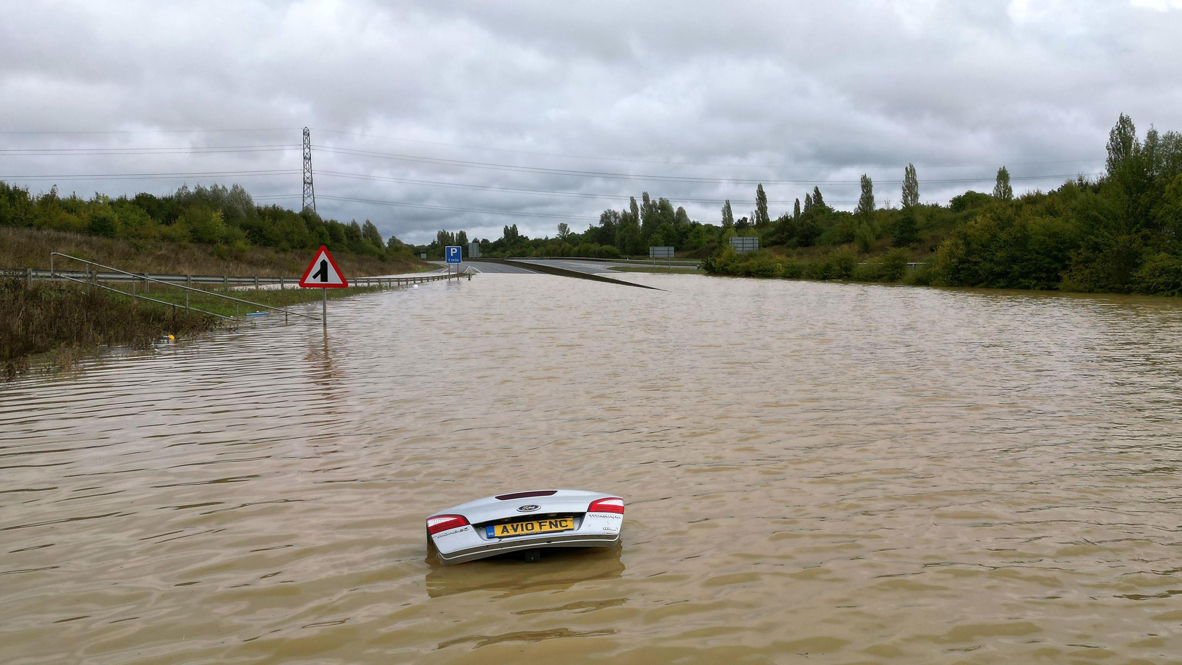 Flood water on a main road. A car's boot in the foreground is poking out the water.