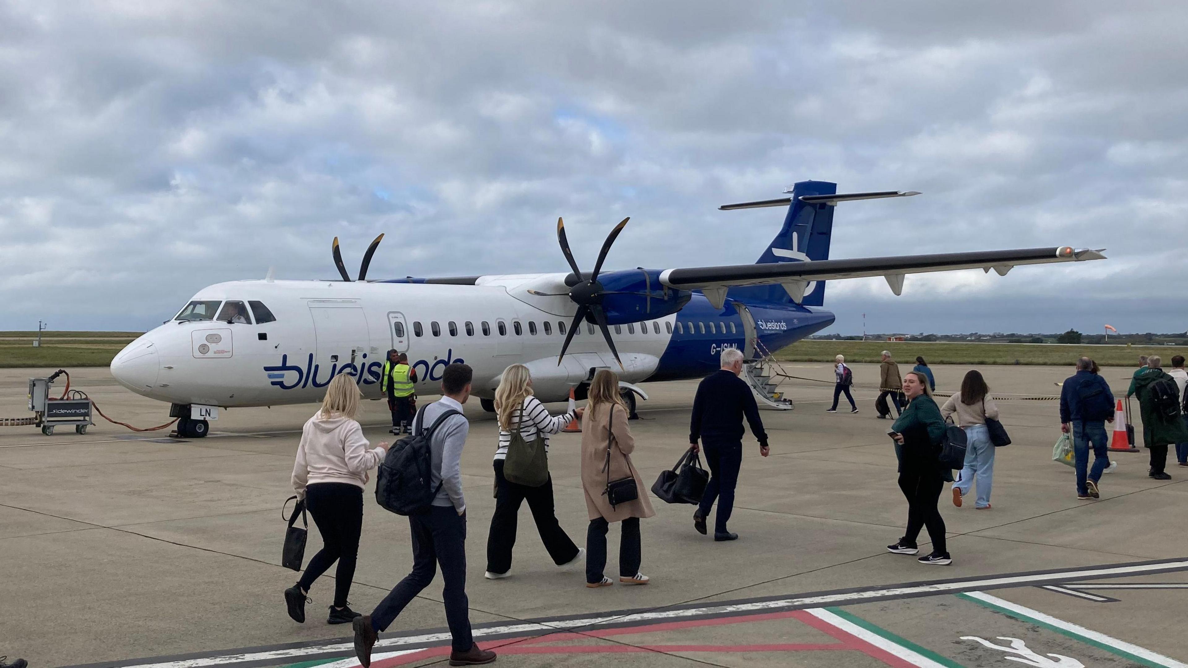 Several passengers walk along the tarmac at an airport as they board a Blue Islands plane.