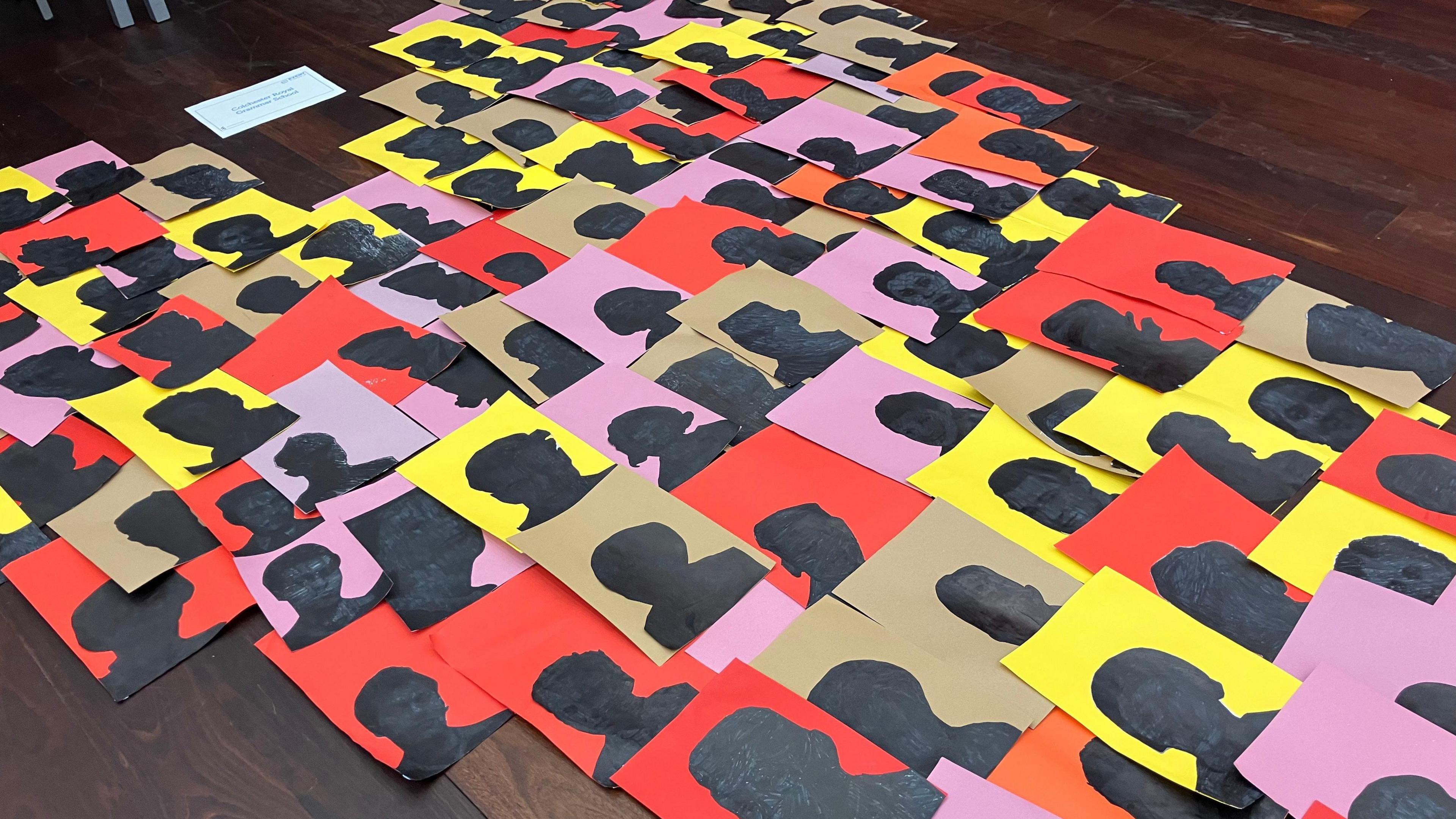 Lots of pictures of faces on different coloured A4 paper sheets arranged on the floor