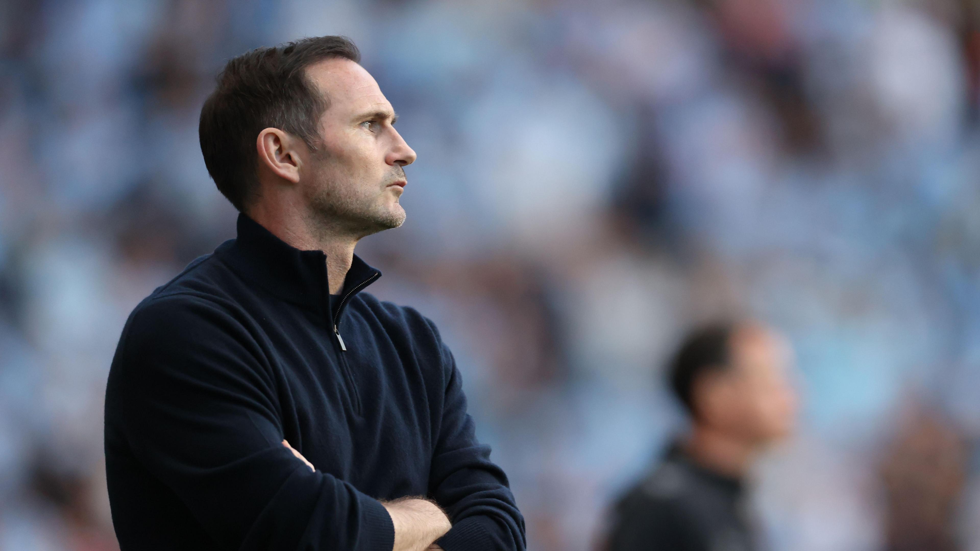 Frank Lampard with his arms folded, watching a match from the touchline