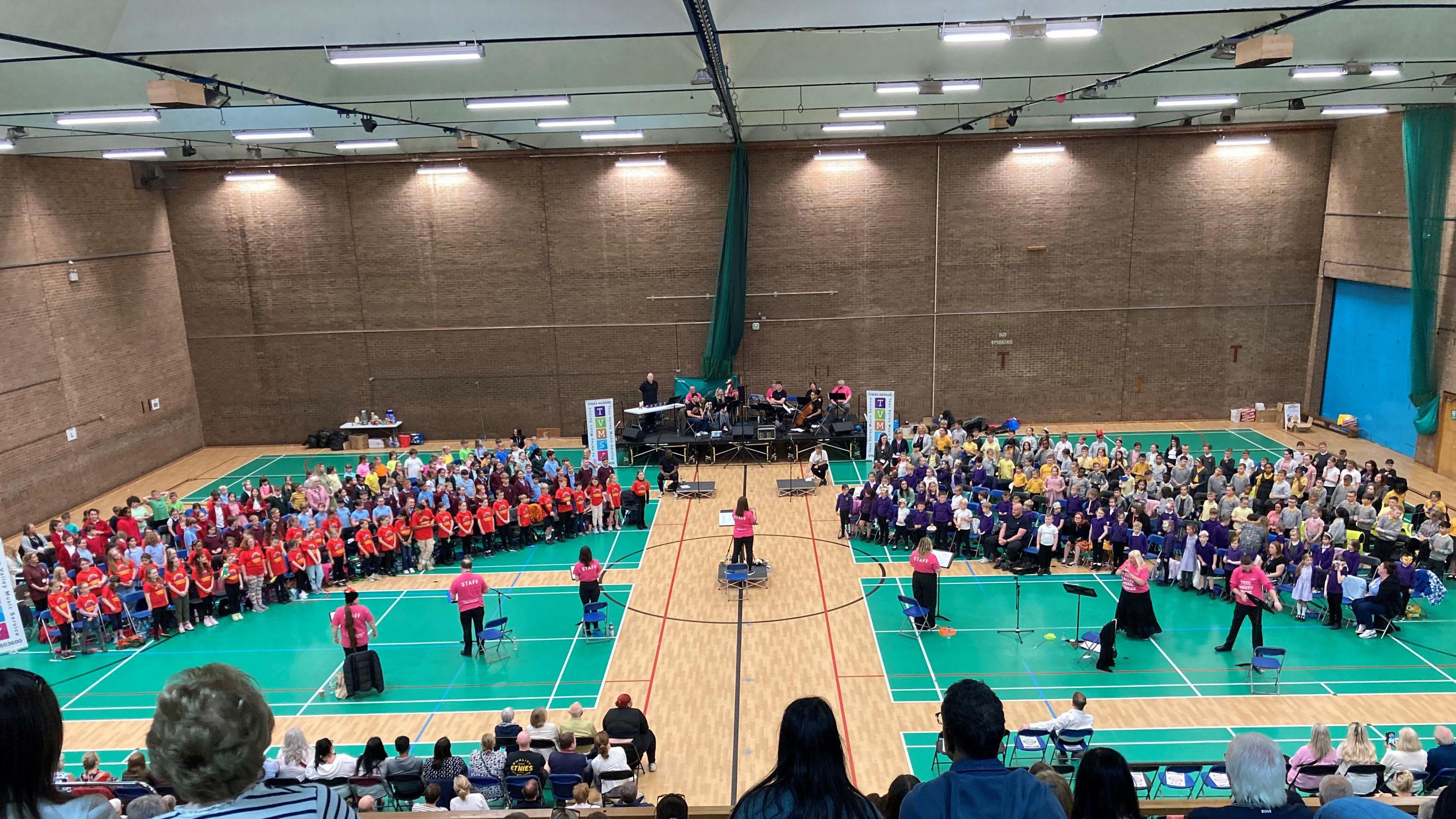 A view of children singing with Royal Opera House musicians performing in the background as parents watch 