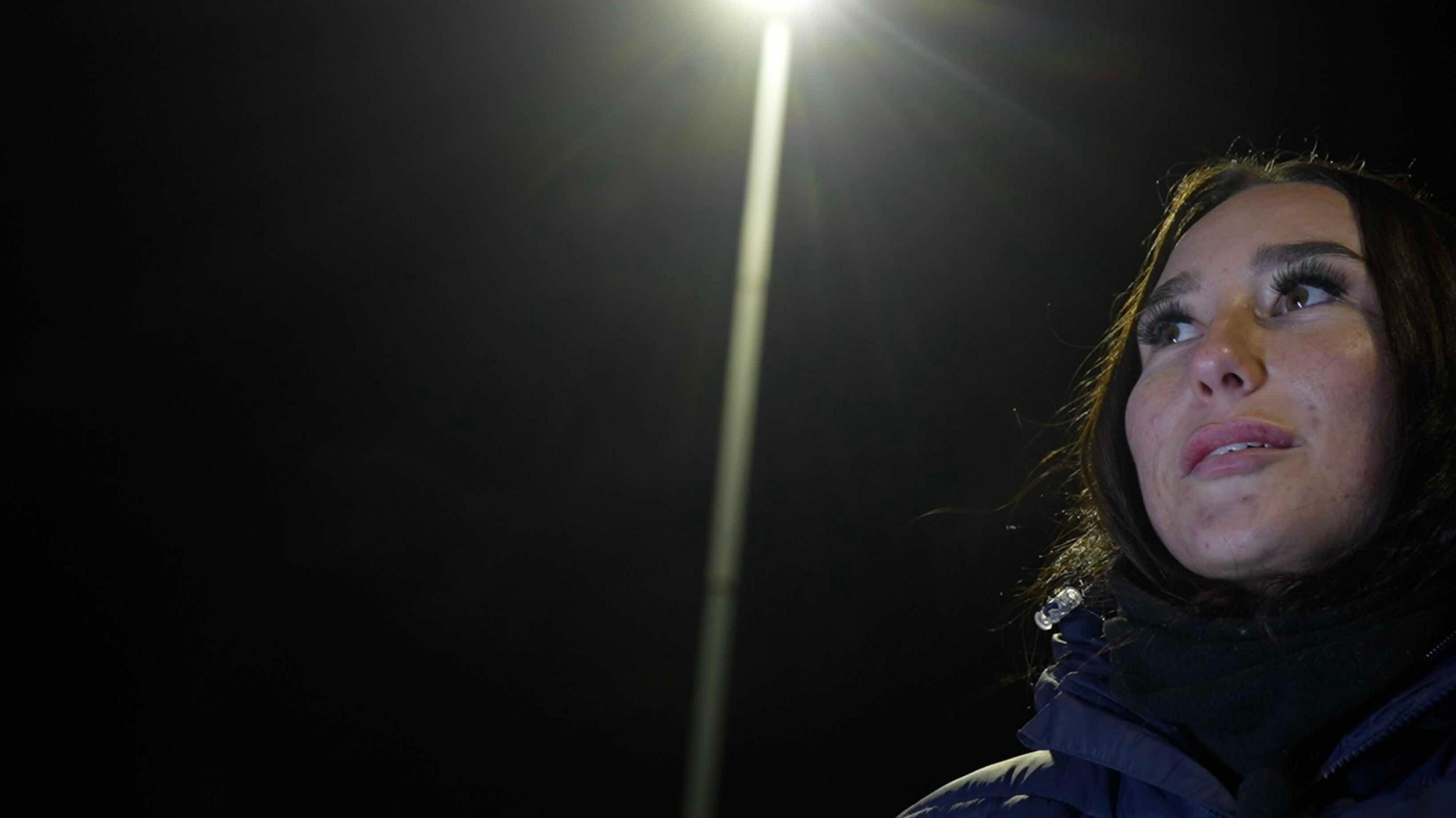 Connolly-Brame looks out onto the training pitch, illuminated by the floodlights on a cold winter's evening. Her breath visible. 