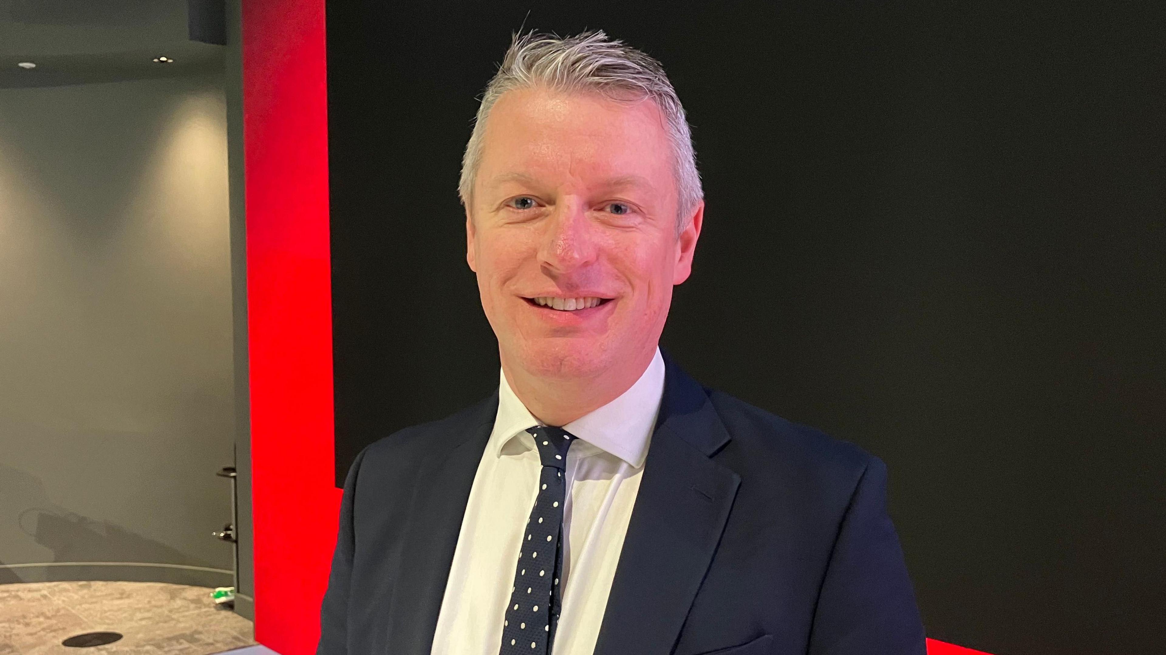 A smiling man with silver hair and a smart suit.