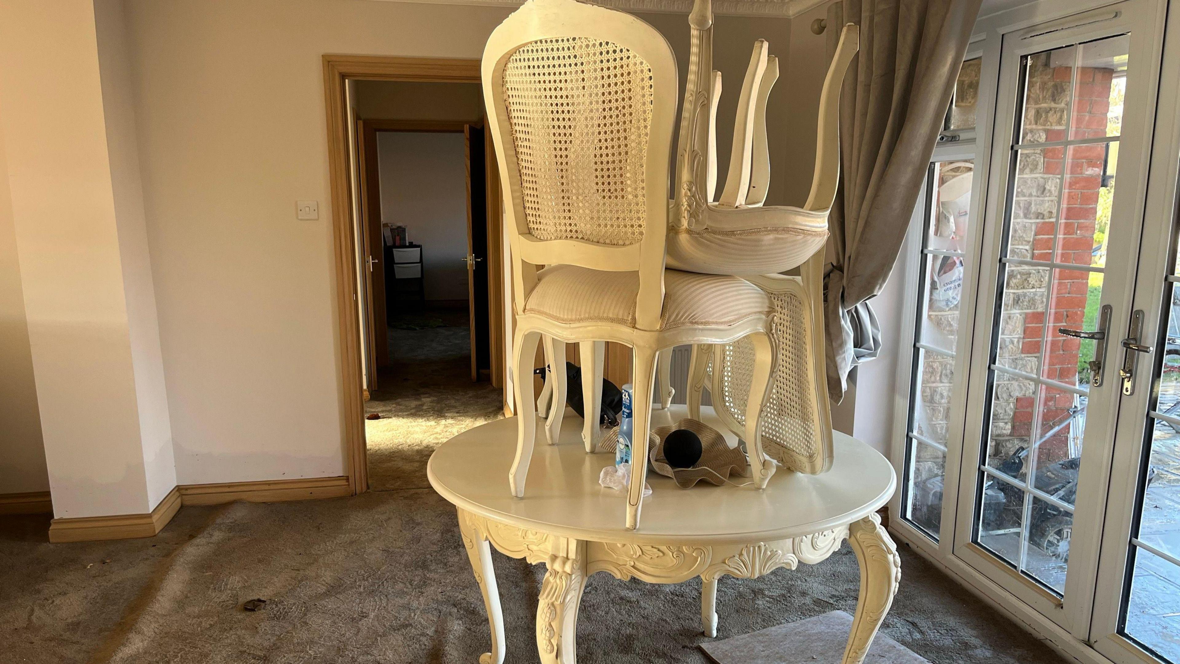 Inside of Jane and Jimmy West's flooded home, showing chairs stacked up on a table which sits on a sodden carpet