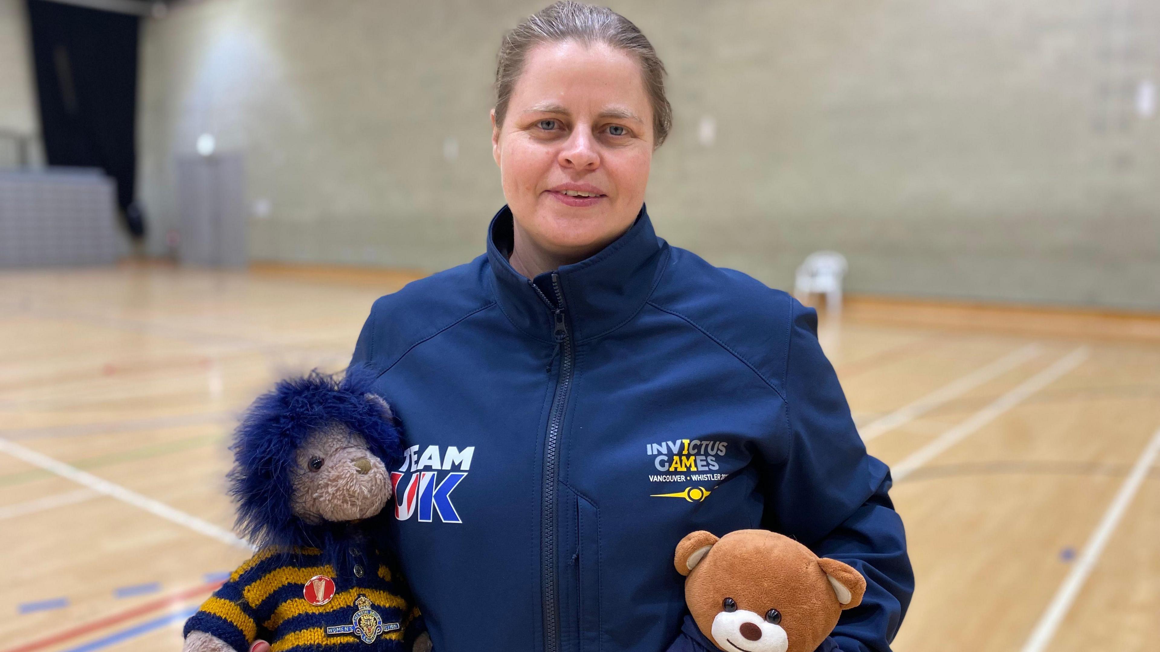 Angela Holland holding two stuffed animals wearing a navy Team UK zip-up jacket