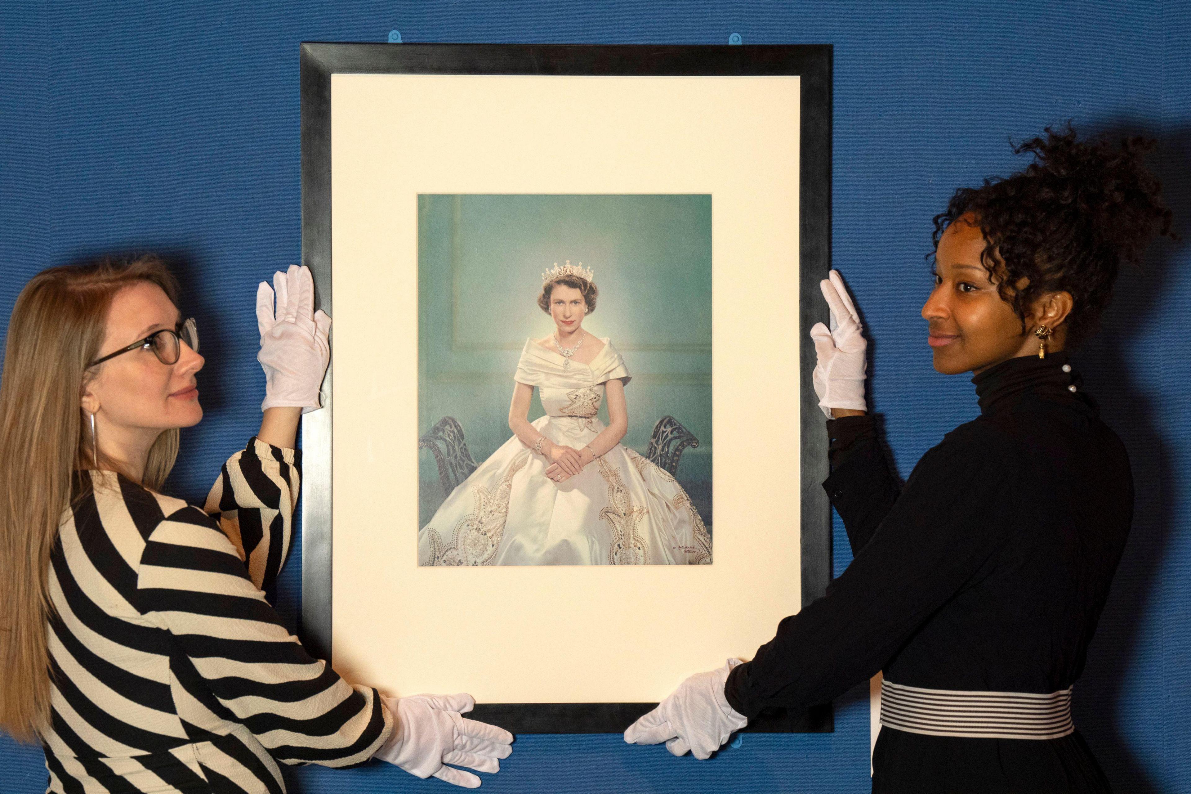 Two curators hold a picture of a picure of Princess Elizabeth who is wearing a white dress. 