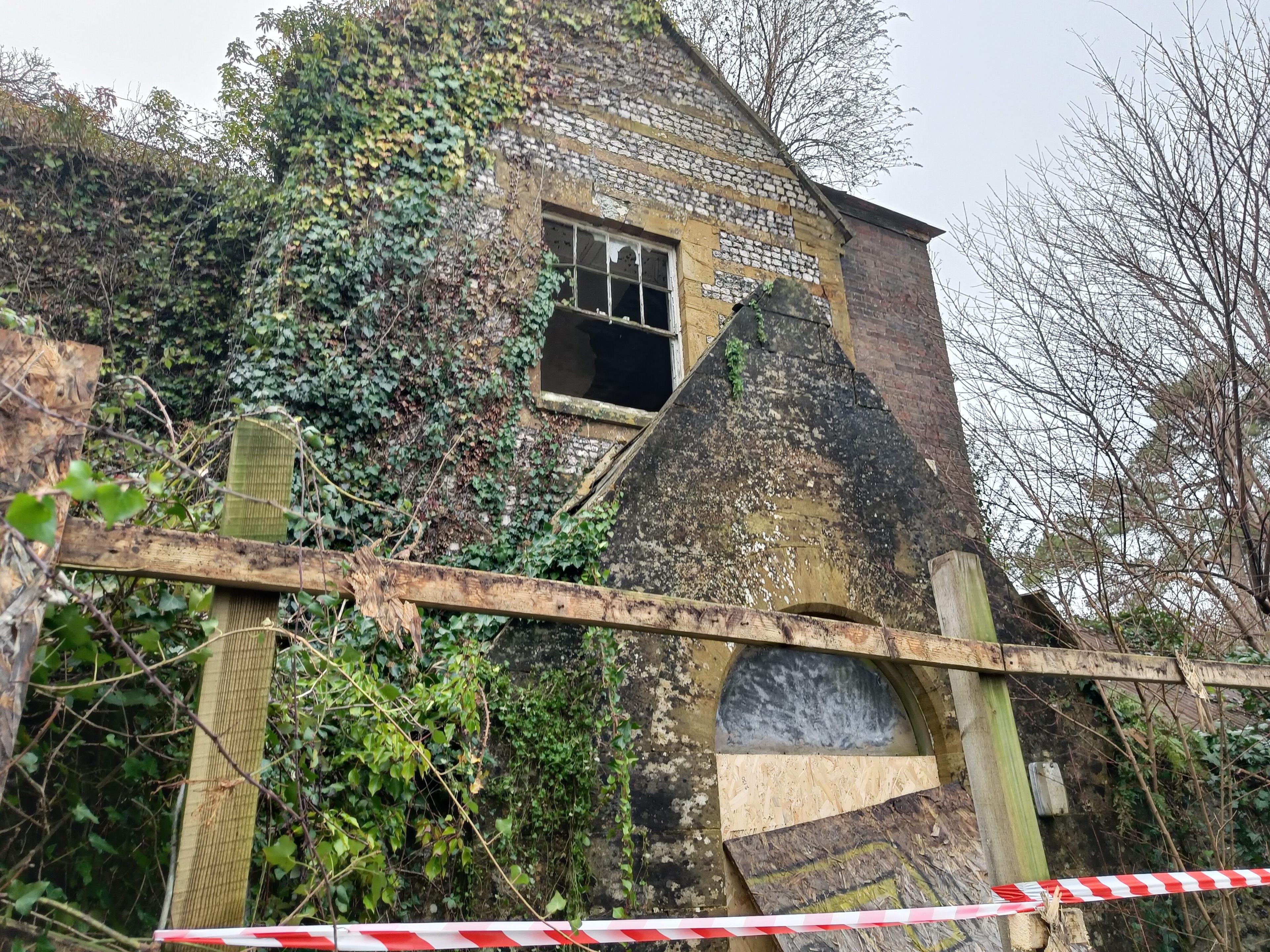 Stone building with foliage growing on its exterior in the daylight. It has been blackened by smoke and looks a touch un-loved.