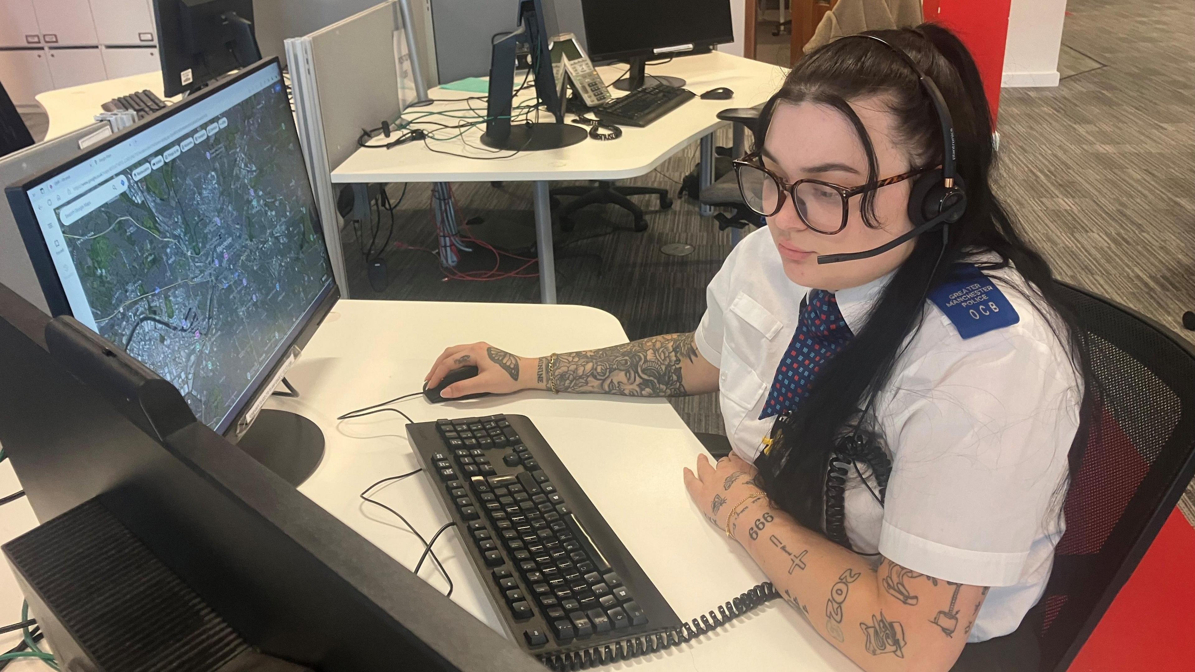 Photograph of a 999 call handler sitting behind her desk at Greater Manchester Police force headquarters.