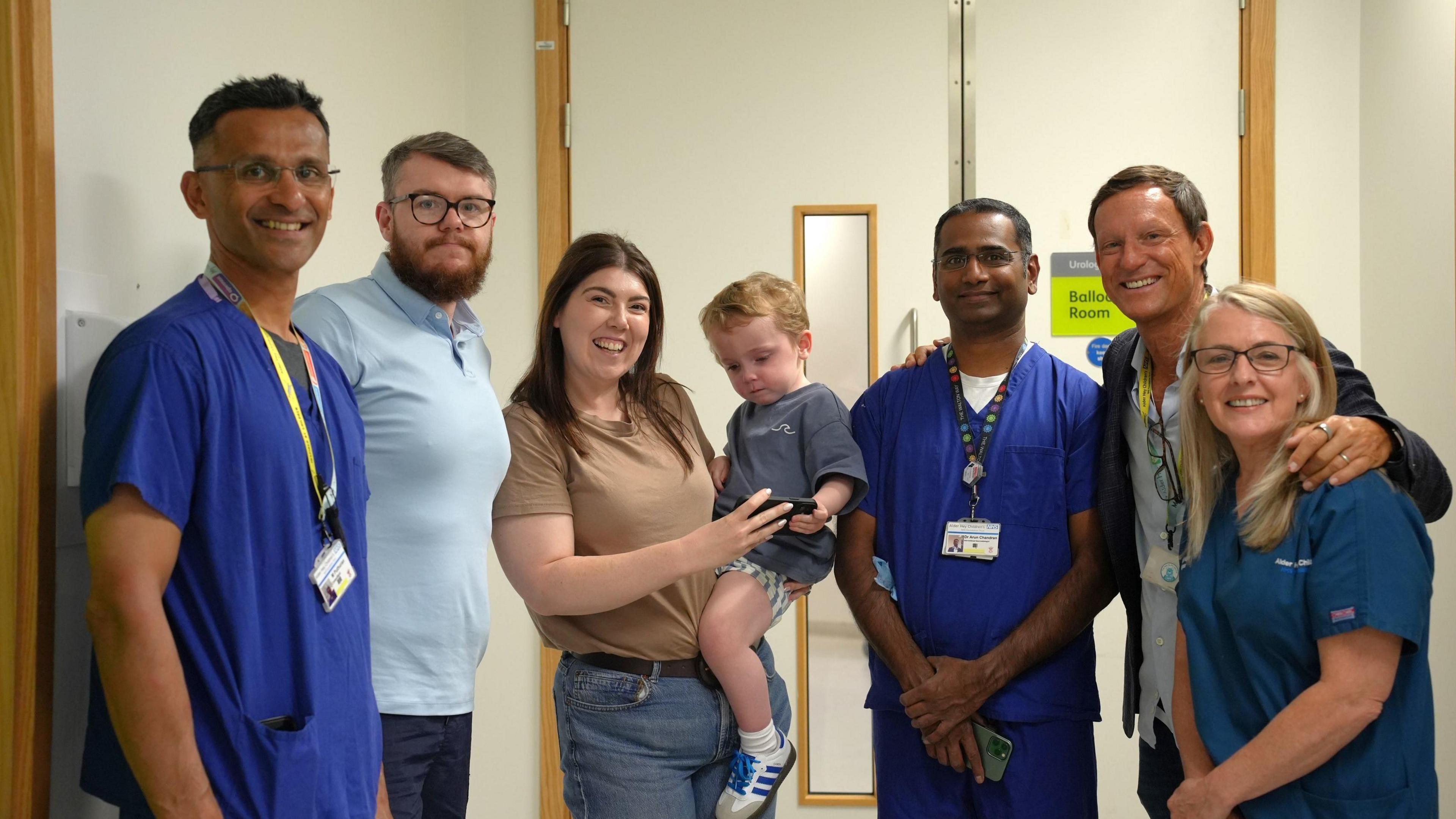 Group picture of Lucy as she holds her son Conor and is surrounded by some of the hospital medics, who are wearing blue scrubs
