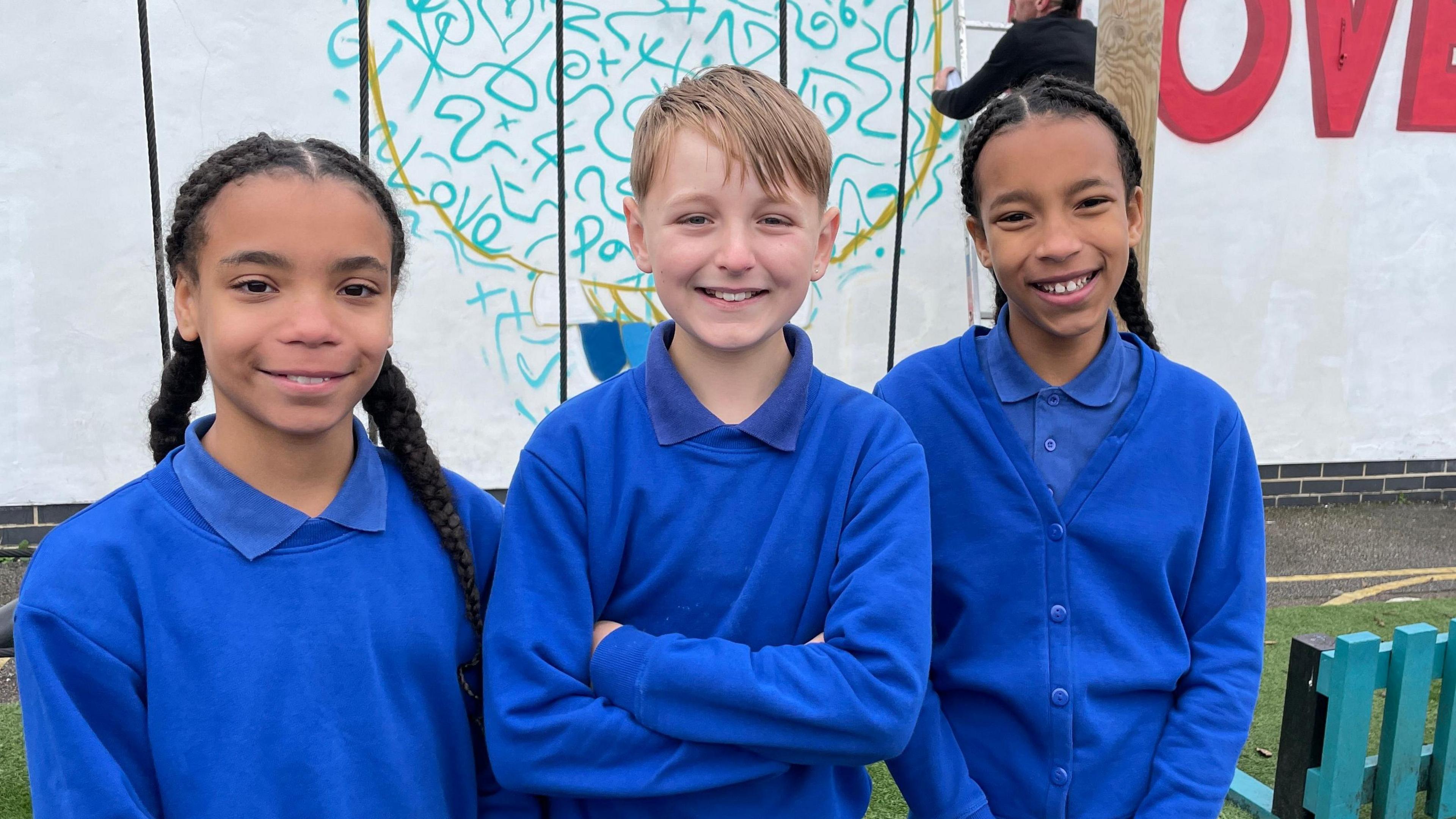 Three pupils in blue uniforms stand in front of Soapspray working on his mural