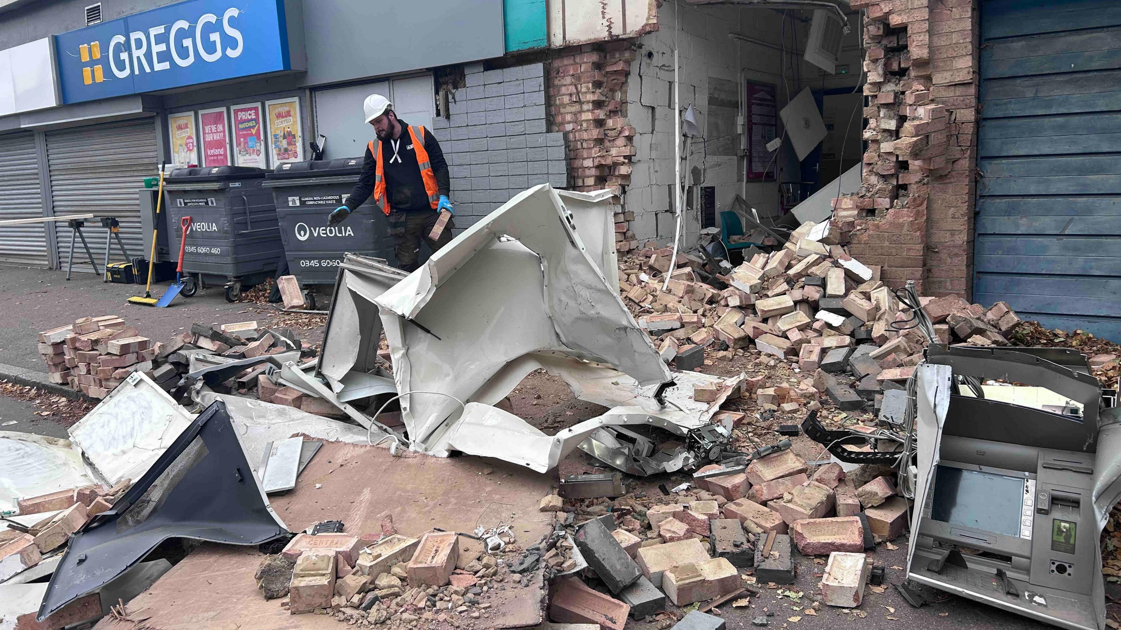The damaged front of a cash machine discarded amongst bricks and rubble after it was ripped from a wall using machinery.