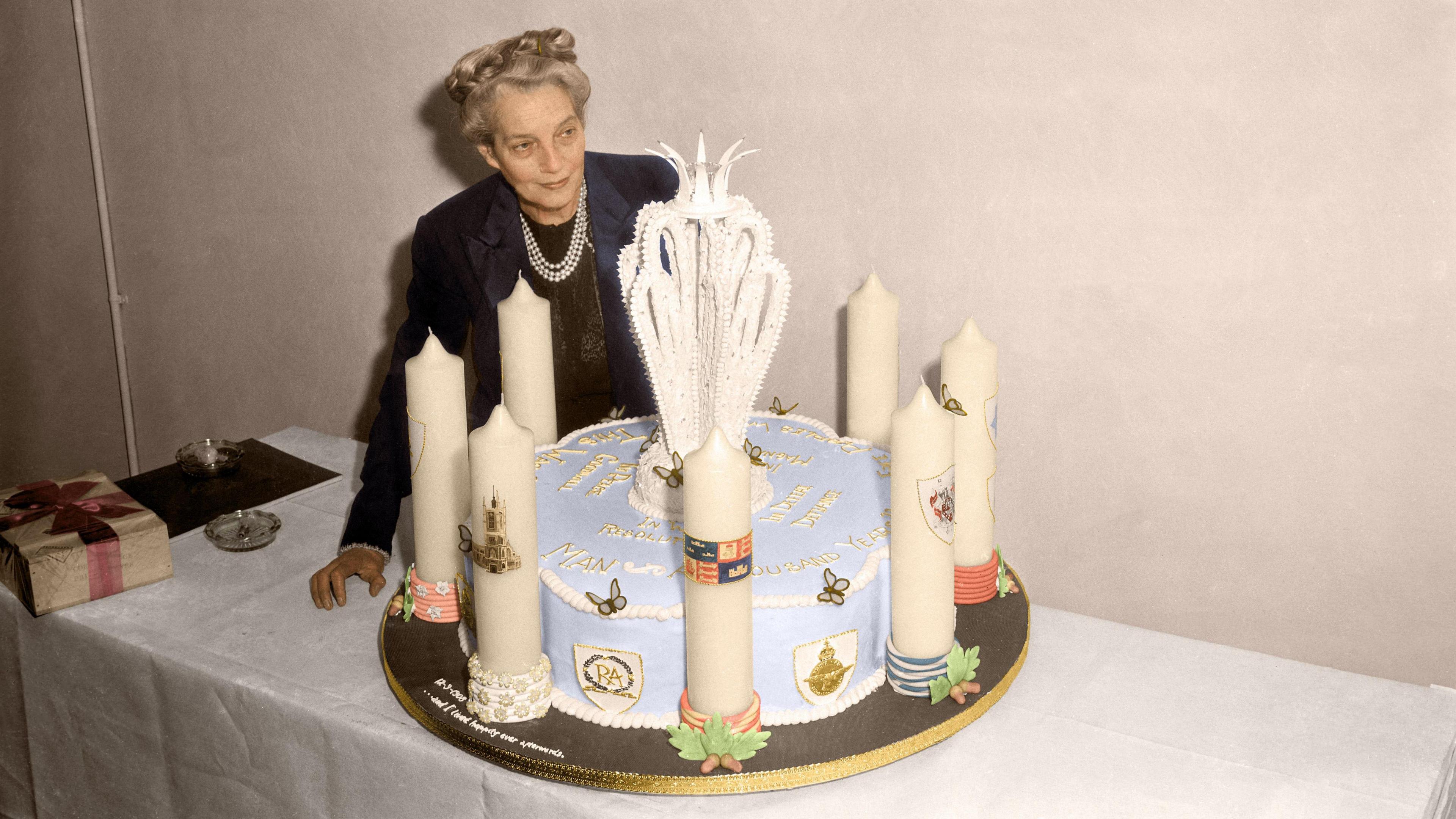 A woman puts a big blue cake down on a table, surrounded by candles for Winston Churchill