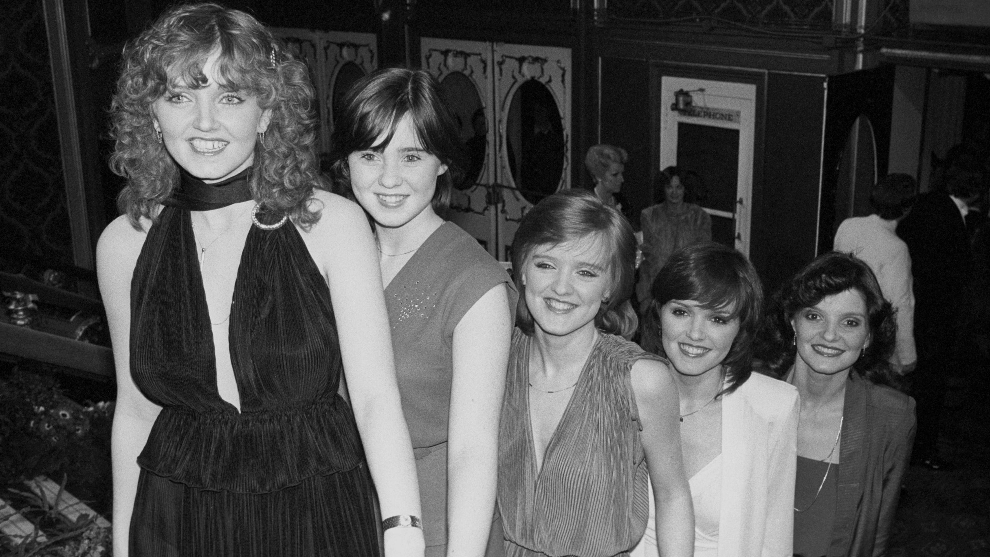 A black and white photo of the five Nolan sisters walking up a staircase inside a theatre