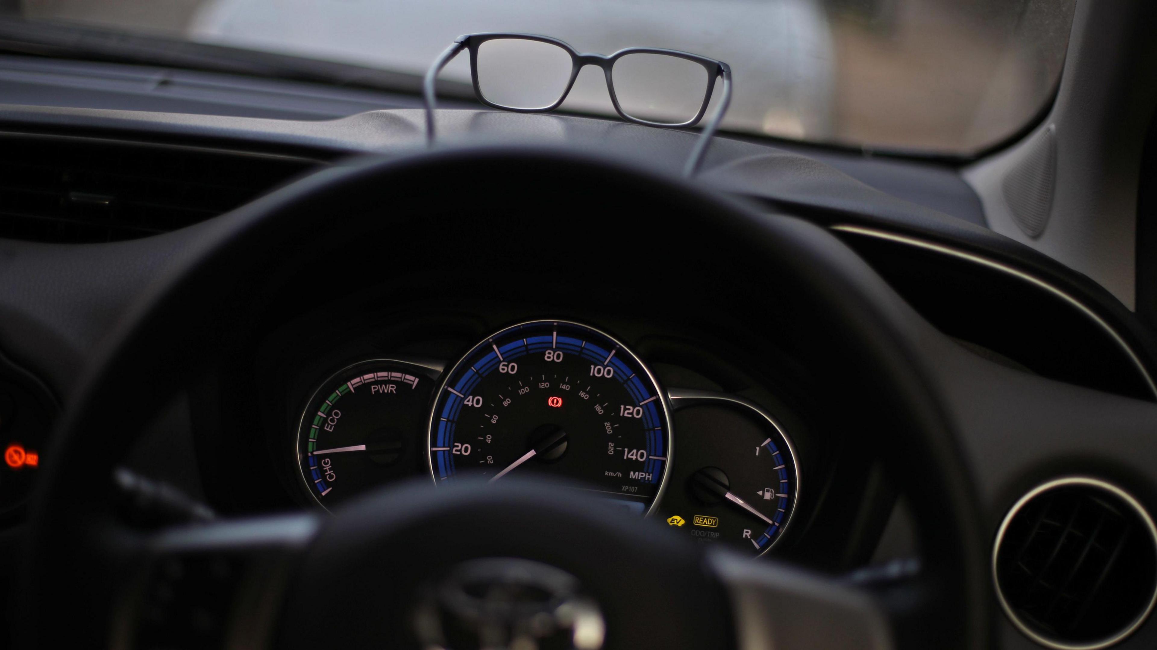 A close-up of a pair of glasses on the dashboard of a car.