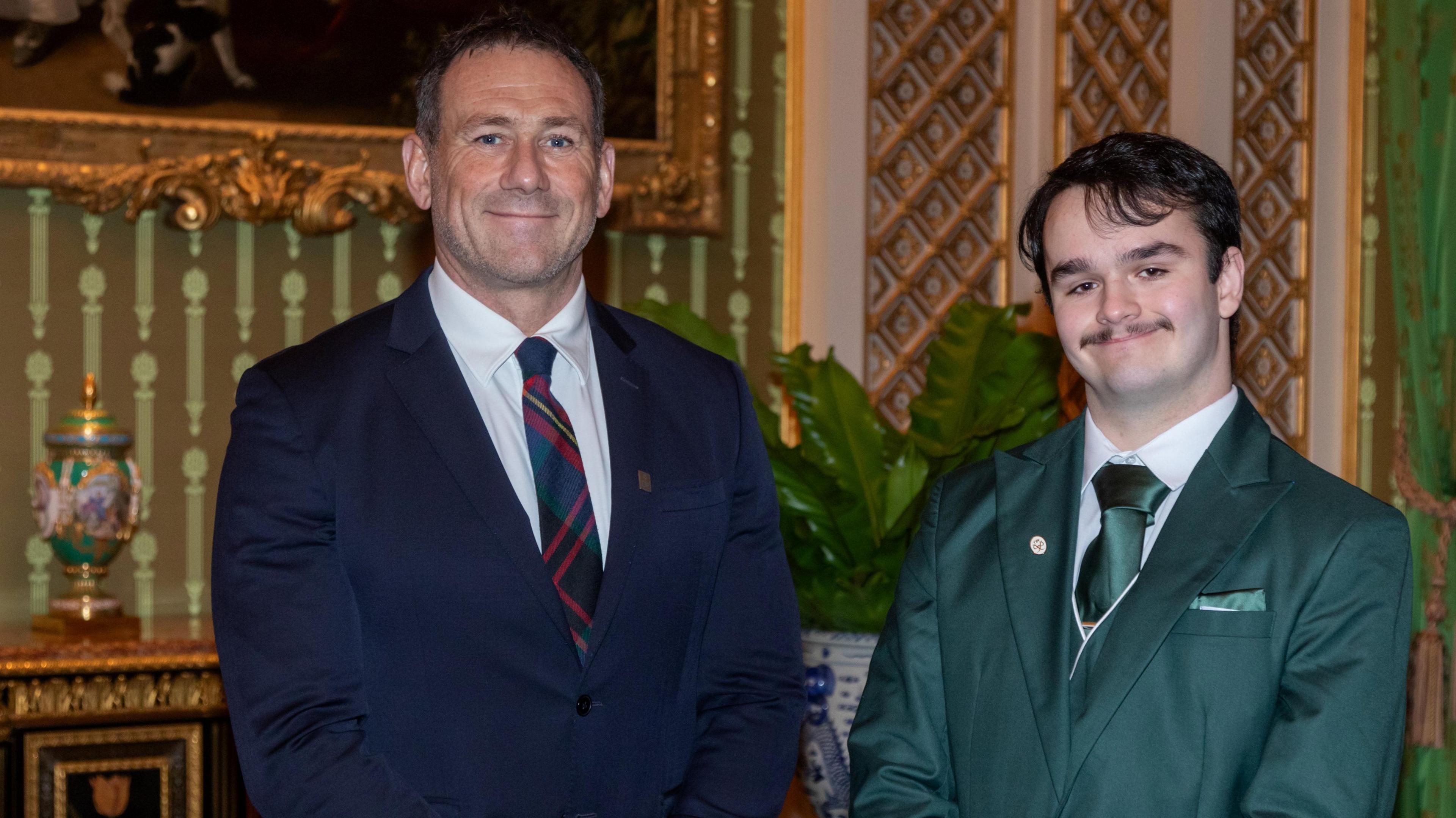 Jason Fox, standing next to Harry Jones, both men are looking straight at the camera and smiling. Jason (left) is wearing a blue suit 