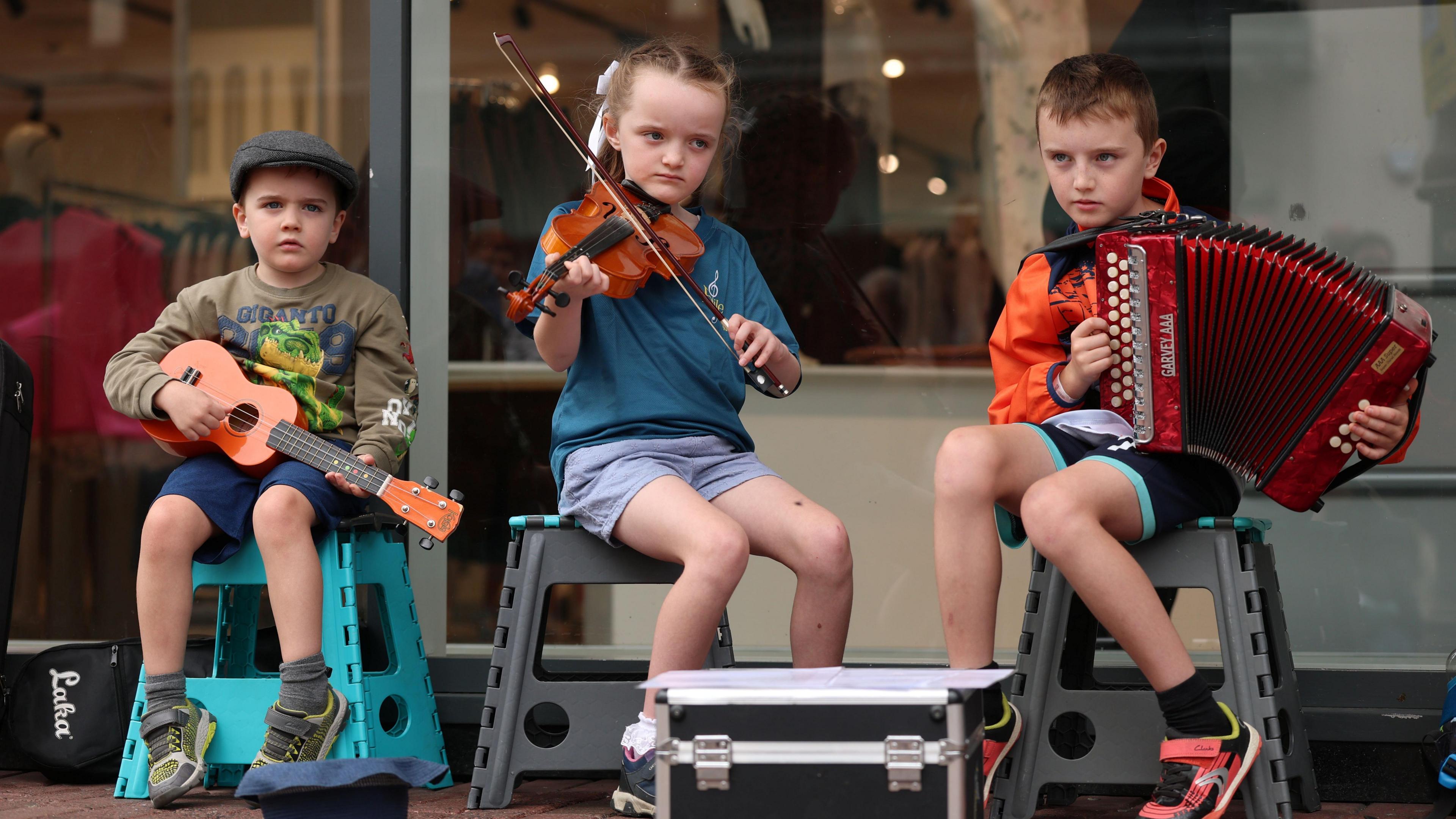 Three children playing music, they are all holding instruments