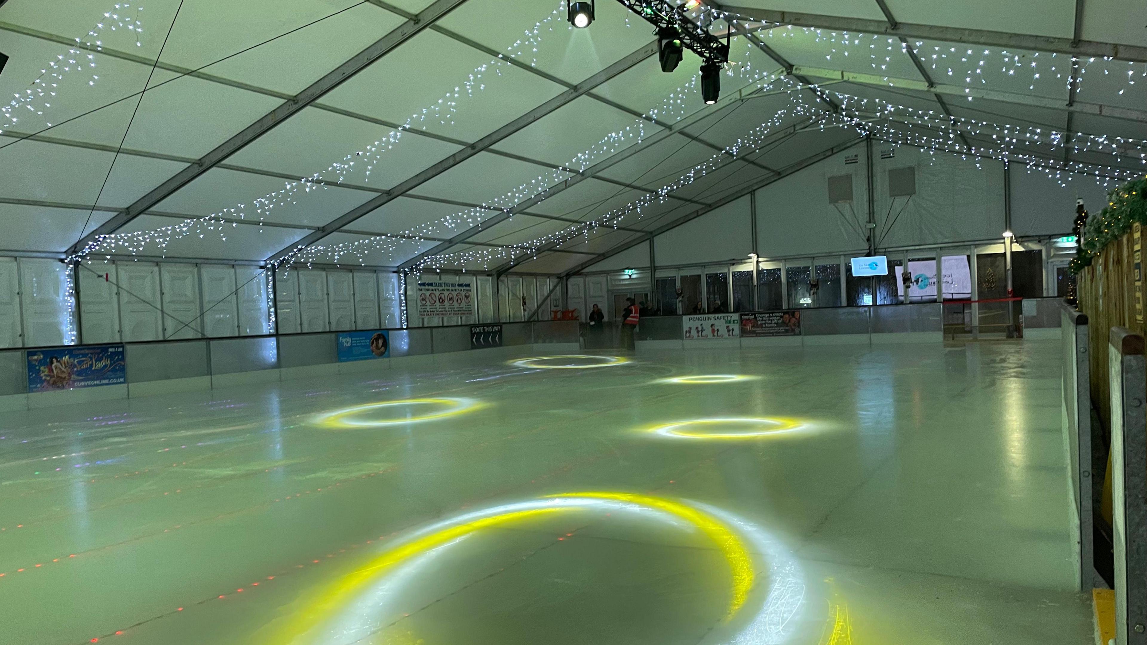 An empty ice rink inside a marquee with lights in the ice and fairy lights at the top of the tent