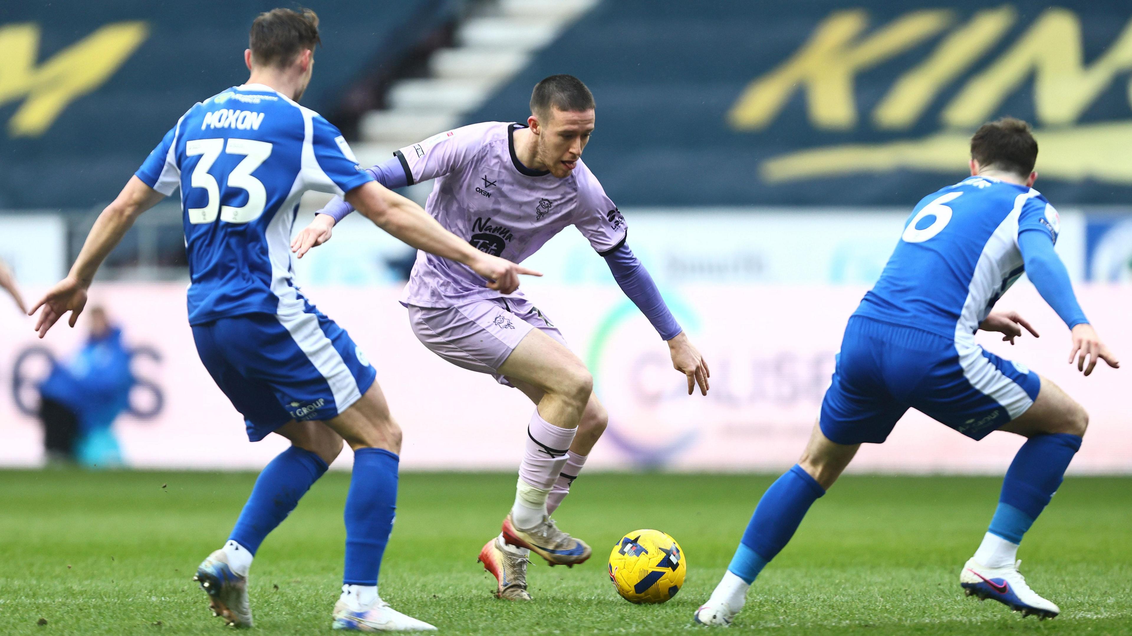 Lincoln player Jack Moylan (centre) is about to shoot as Wigan duo Owen Moxon (33, left) and Jenson Weir (6, right) watch on 