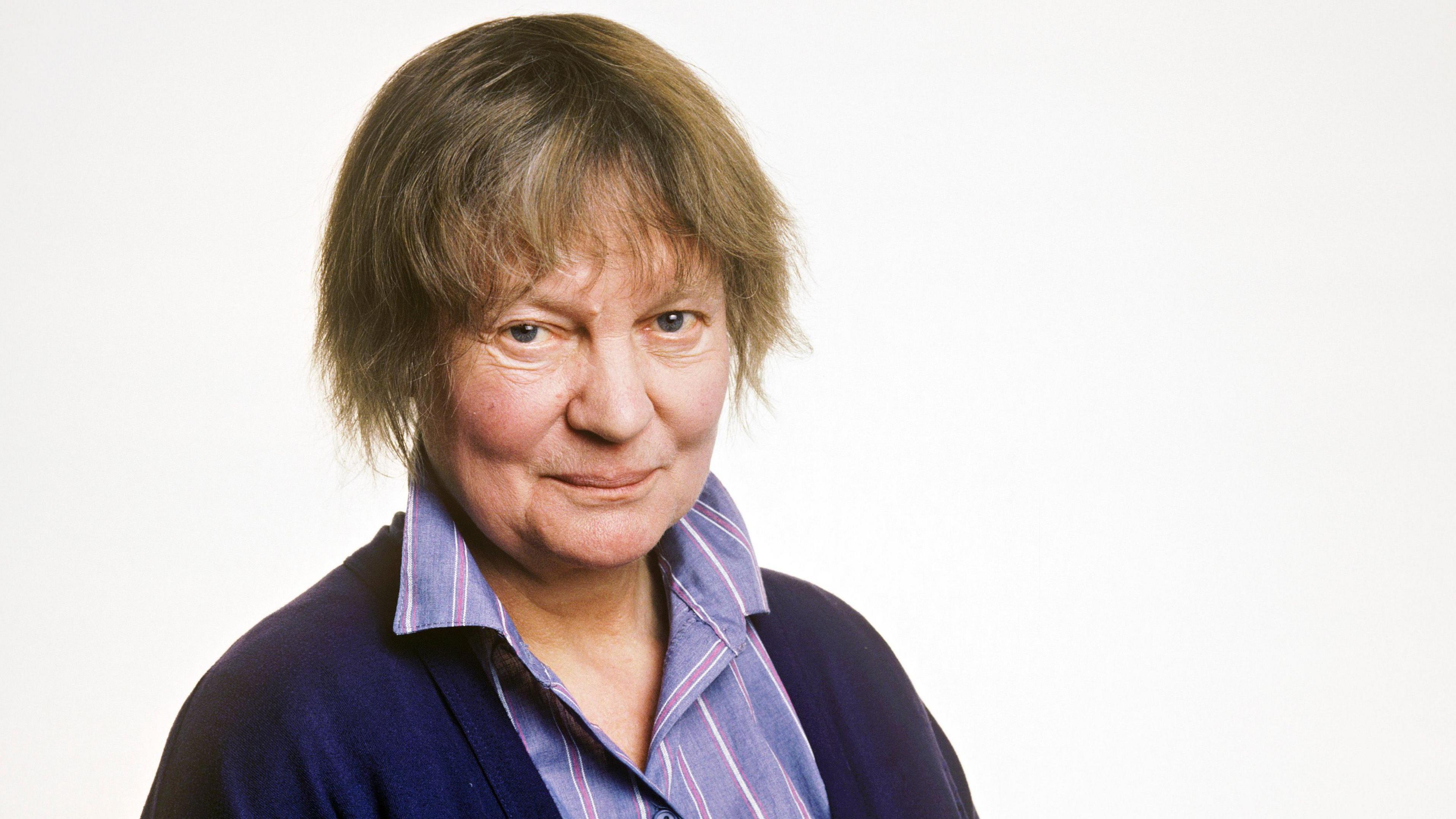 A photograph of Iris Murdoch from the 1980s as part of a photoshoot for one of her books. She is looking at the camera, smiling.