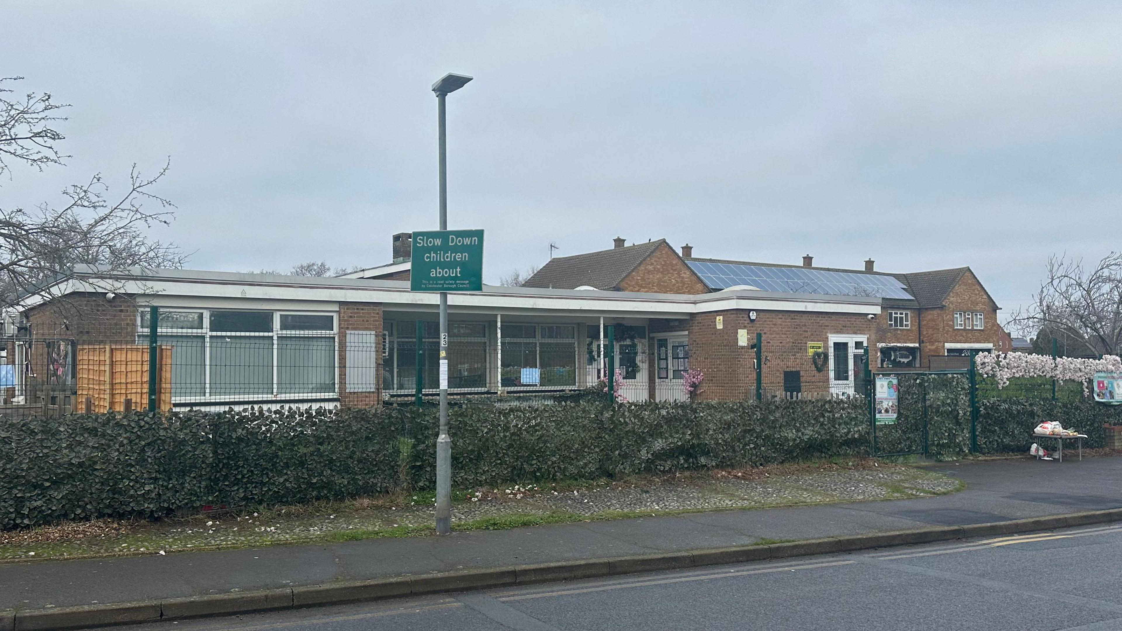 A general view of Blossom preschool in Colchester. The school is single storey and is surrounded by a large gate. A playground sits directly outside the school's entrance.