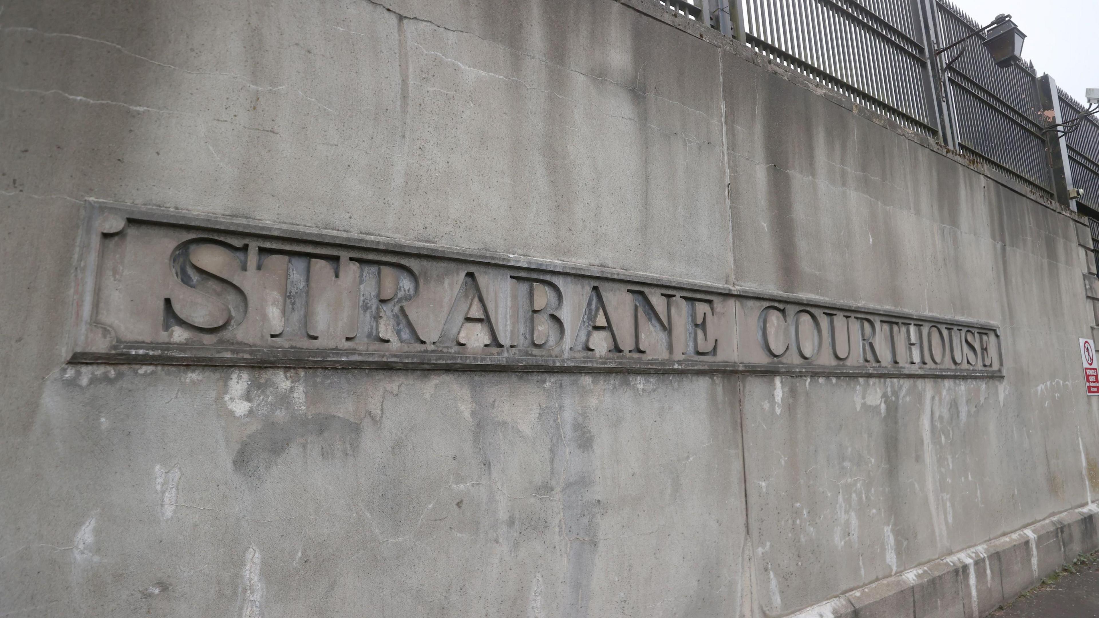 A grey wall with a sign saying Strabane Courthouse. There's a fence on top of the wall with lanterns.