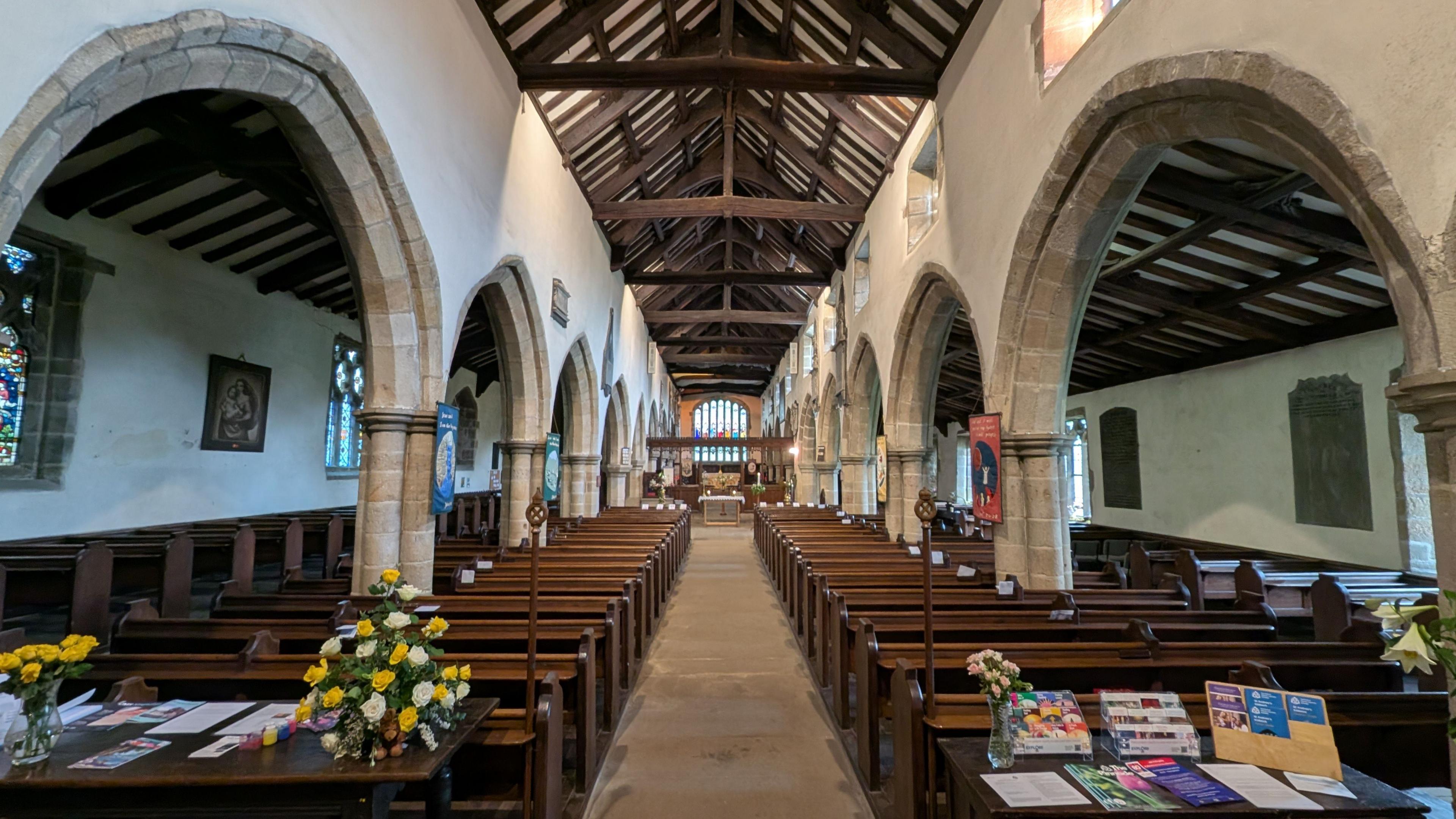 Inside St Andrew's Church in Kildwick North Yorkshire, it has low stone arches and a beamed roof with rows of wooden pews