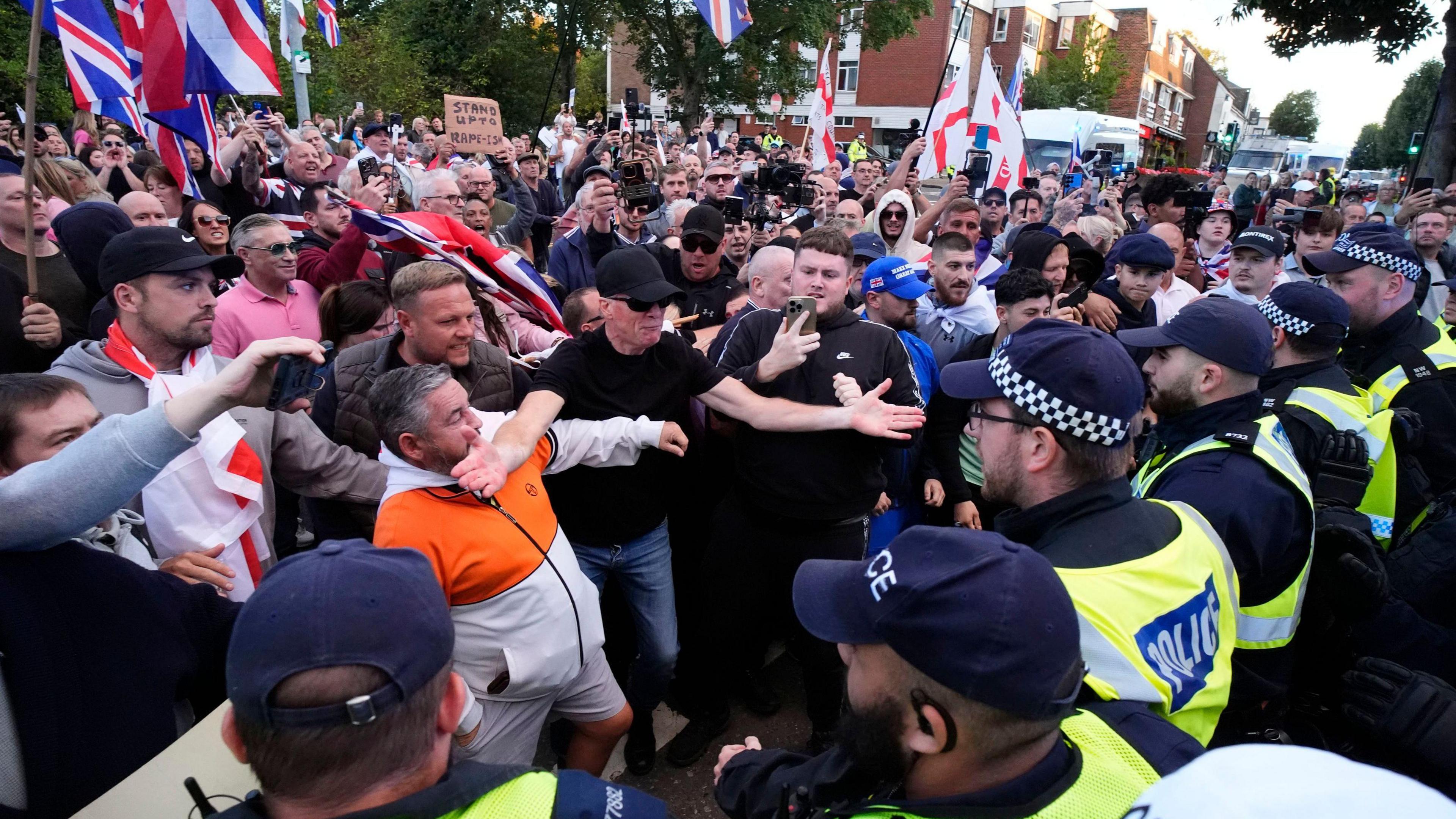 A large crowd of demonstrators, some of whom are waving flags and signs, get close to a line of police officers during a protest march.