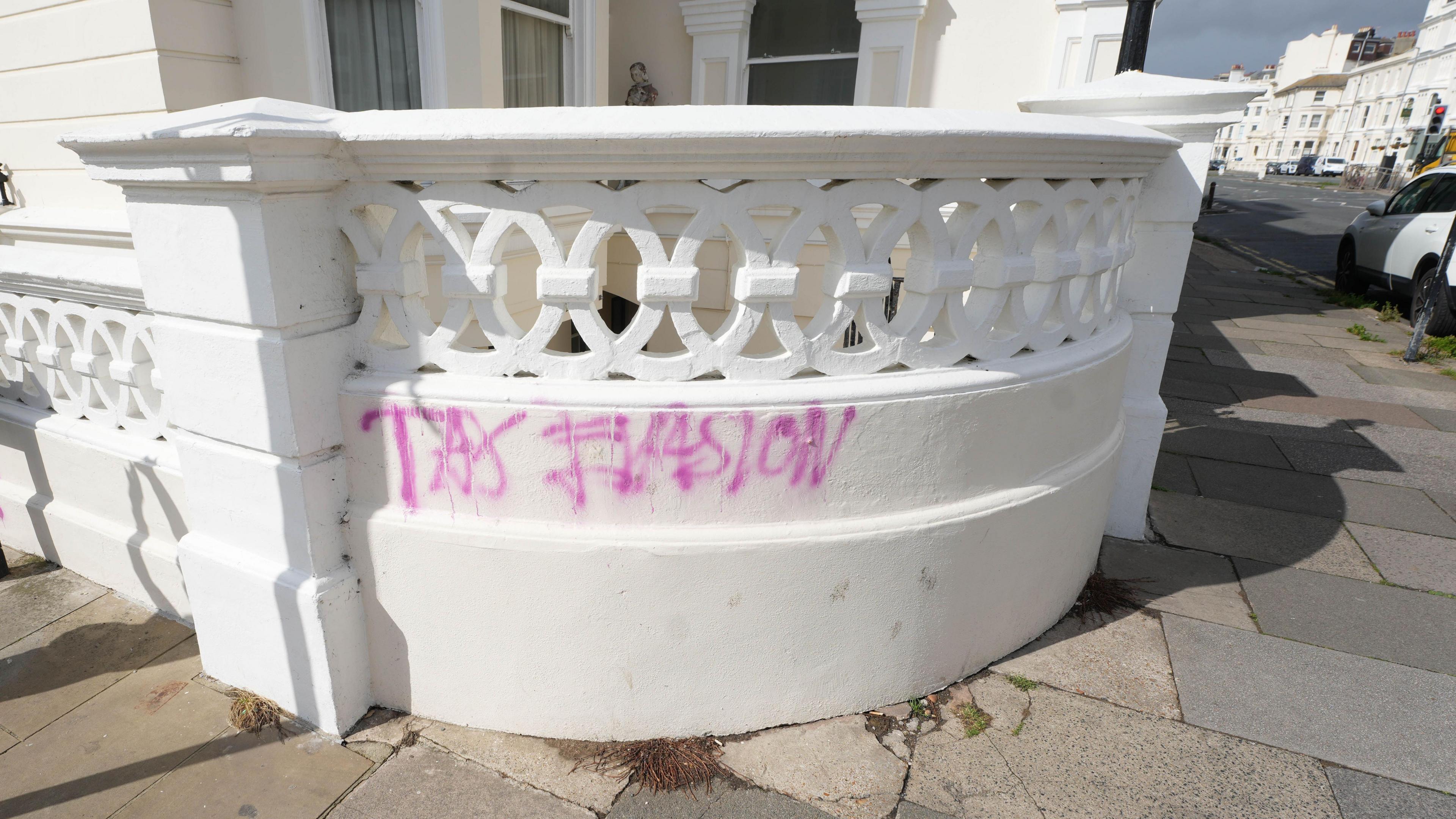 A white wall outside a house with the word "tax evasion" wrote in pink on it