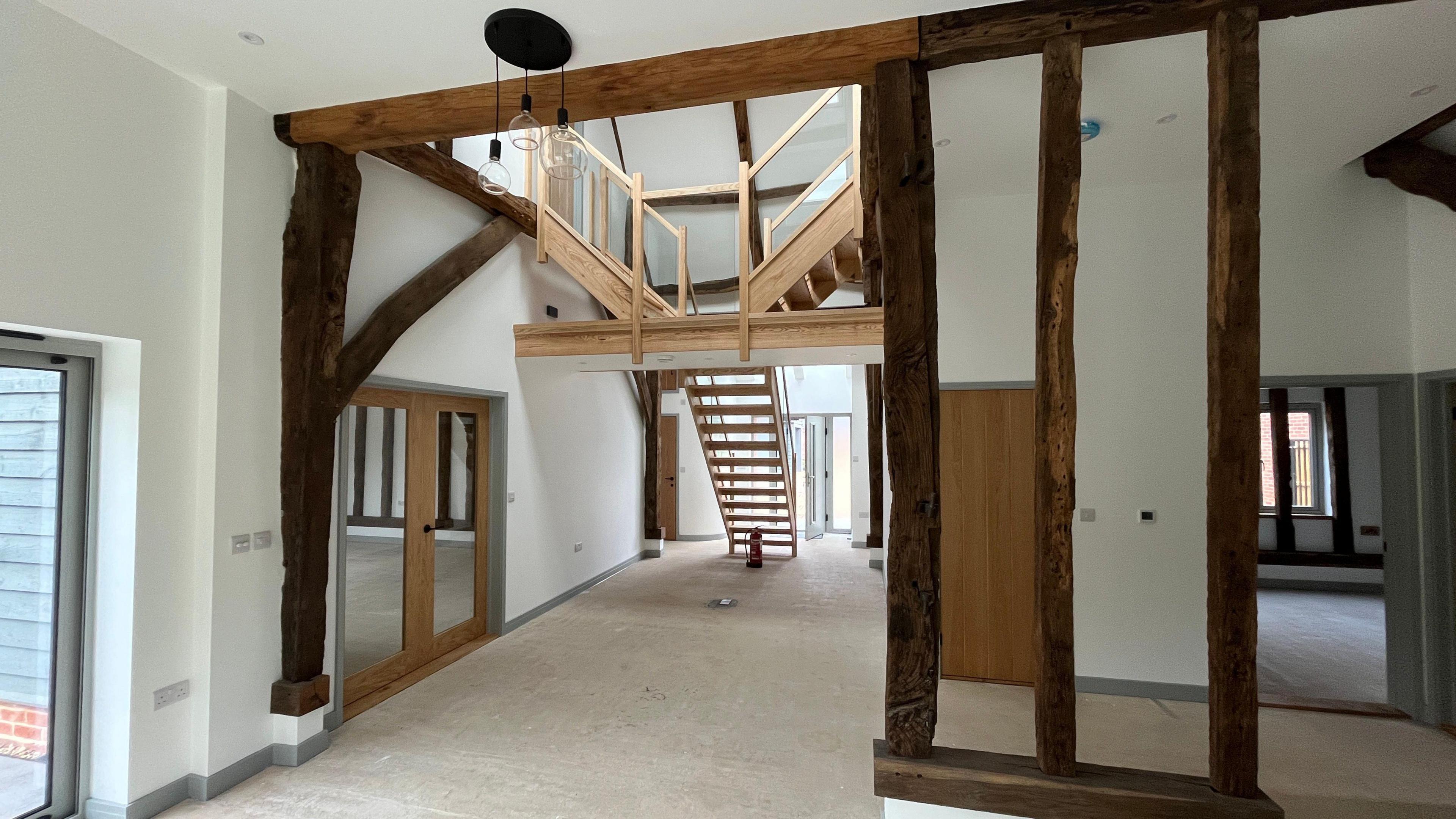 A look inside part of the converted barn home. Wooden beams can be seen around the roof as well as a wooden staircase.