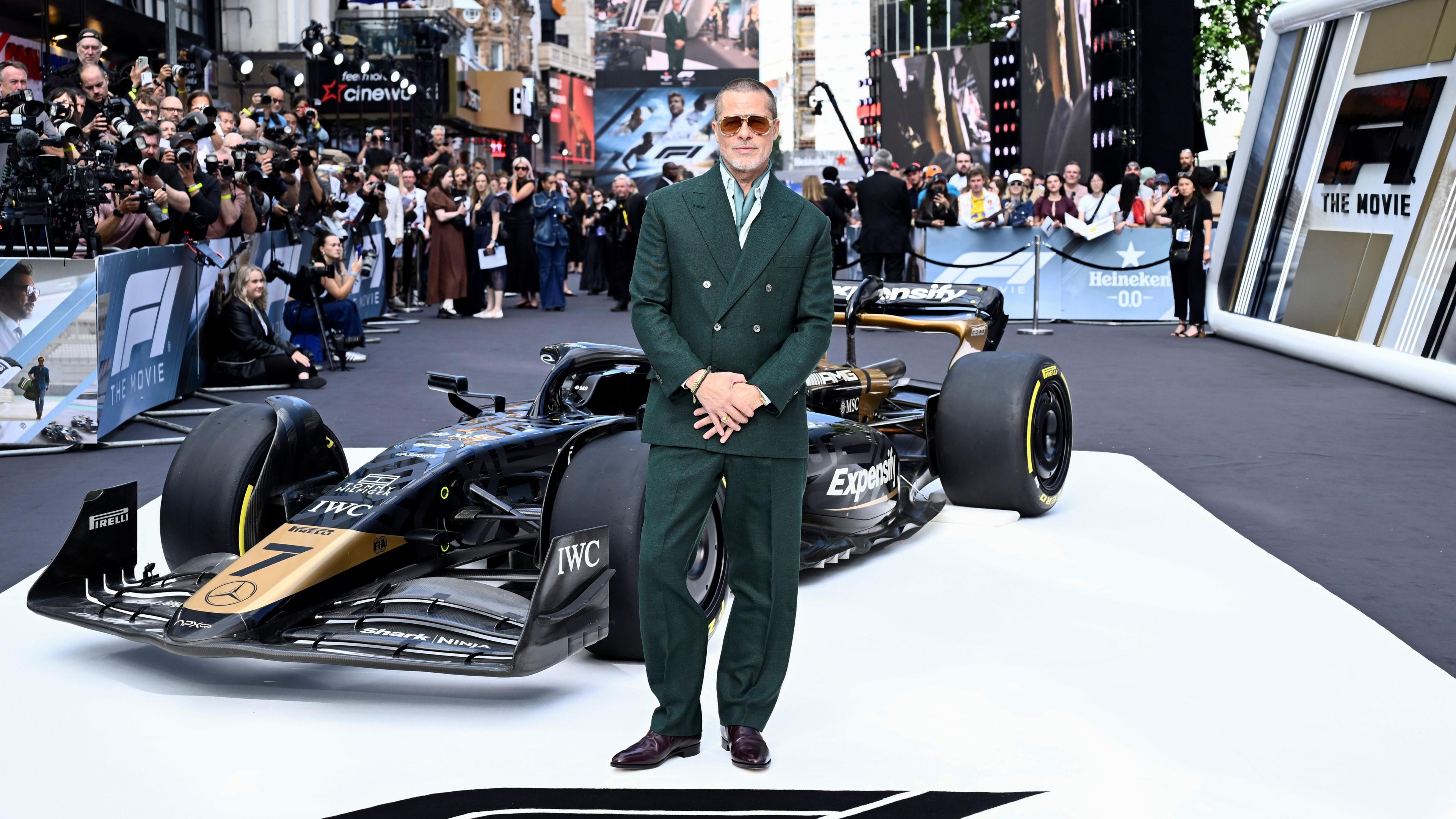 Brad Pitt standing in front of a black and gold F1 car at a movie premiere.