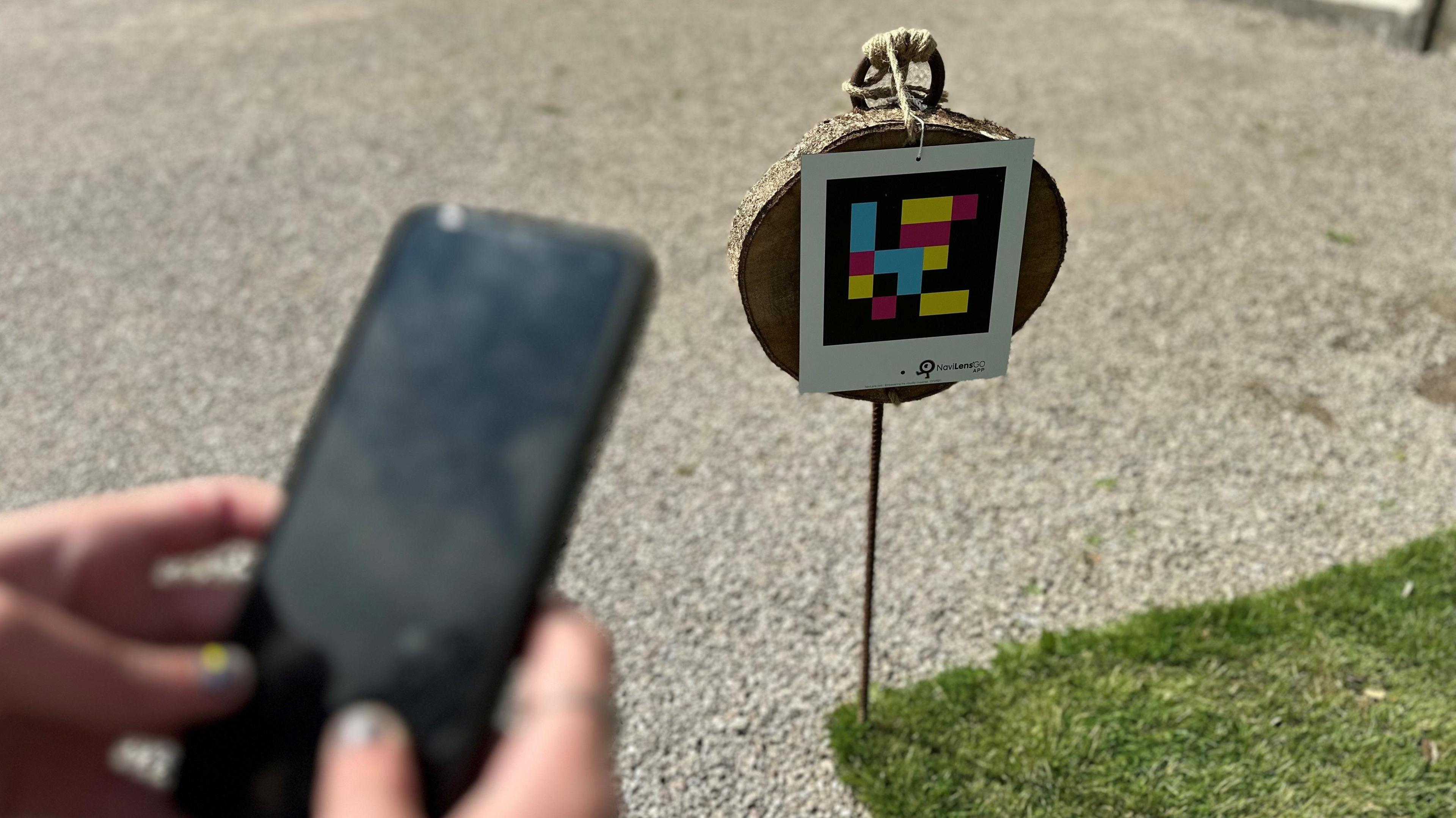 A person holds their phone near a NaviLens QR code located in the Saltram National Trust property's garden.