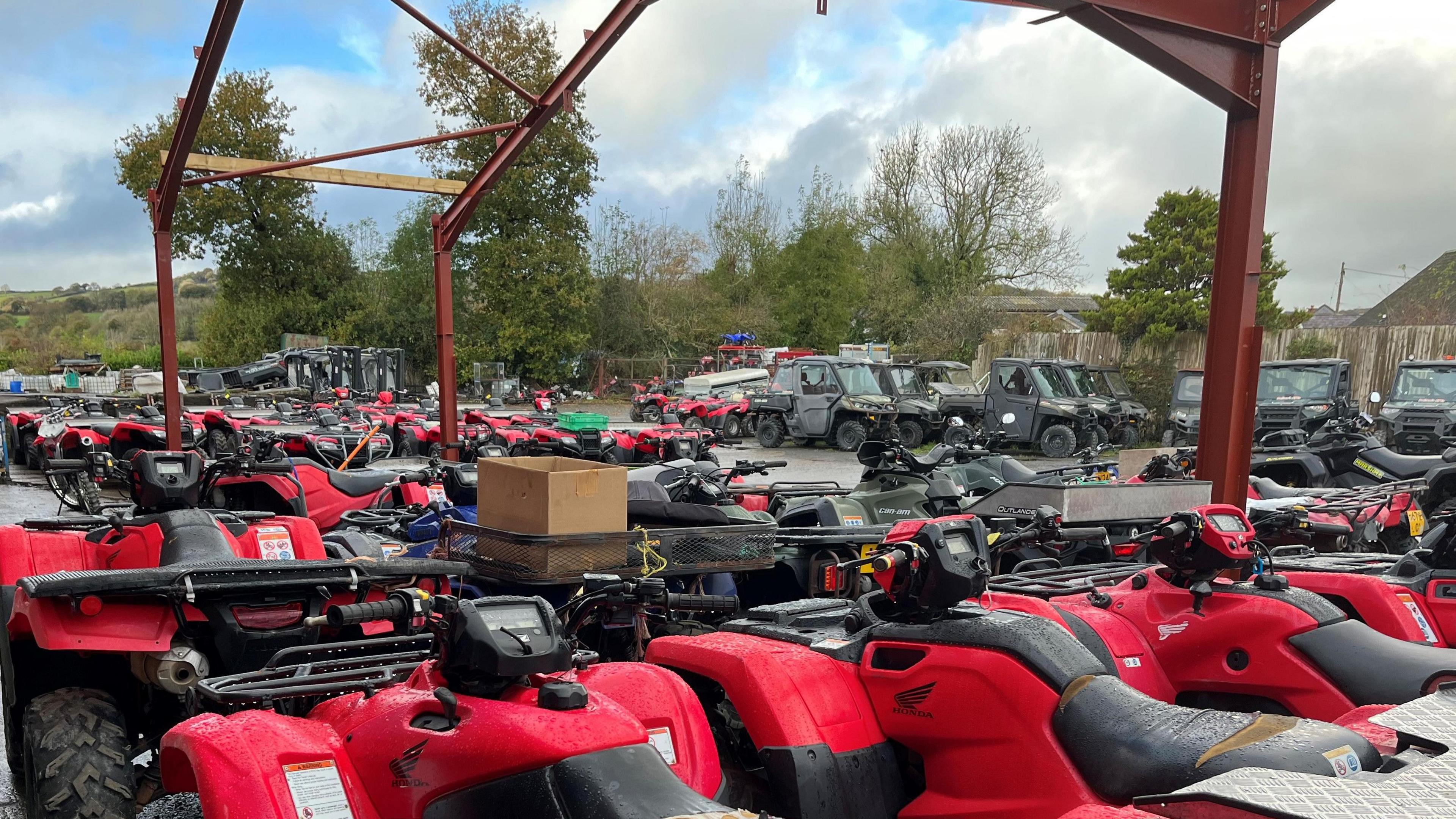 Rows of largely red quad bikes at Dalton ATVs, with other vehicles in the background