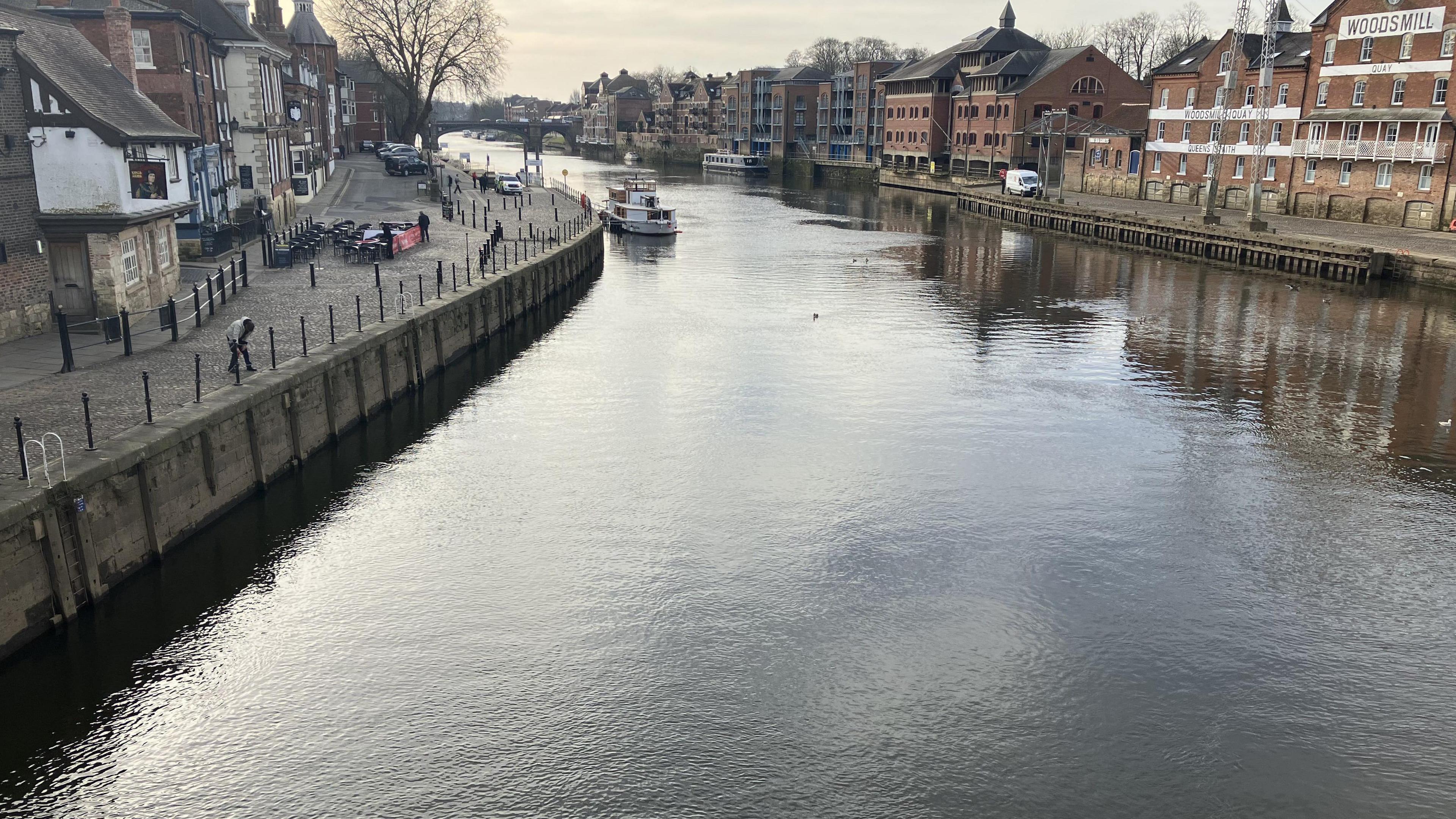 The River Ouse in York, pictured from a bridge. A boat can be seen in the distance. Properties flank the river on both sides.