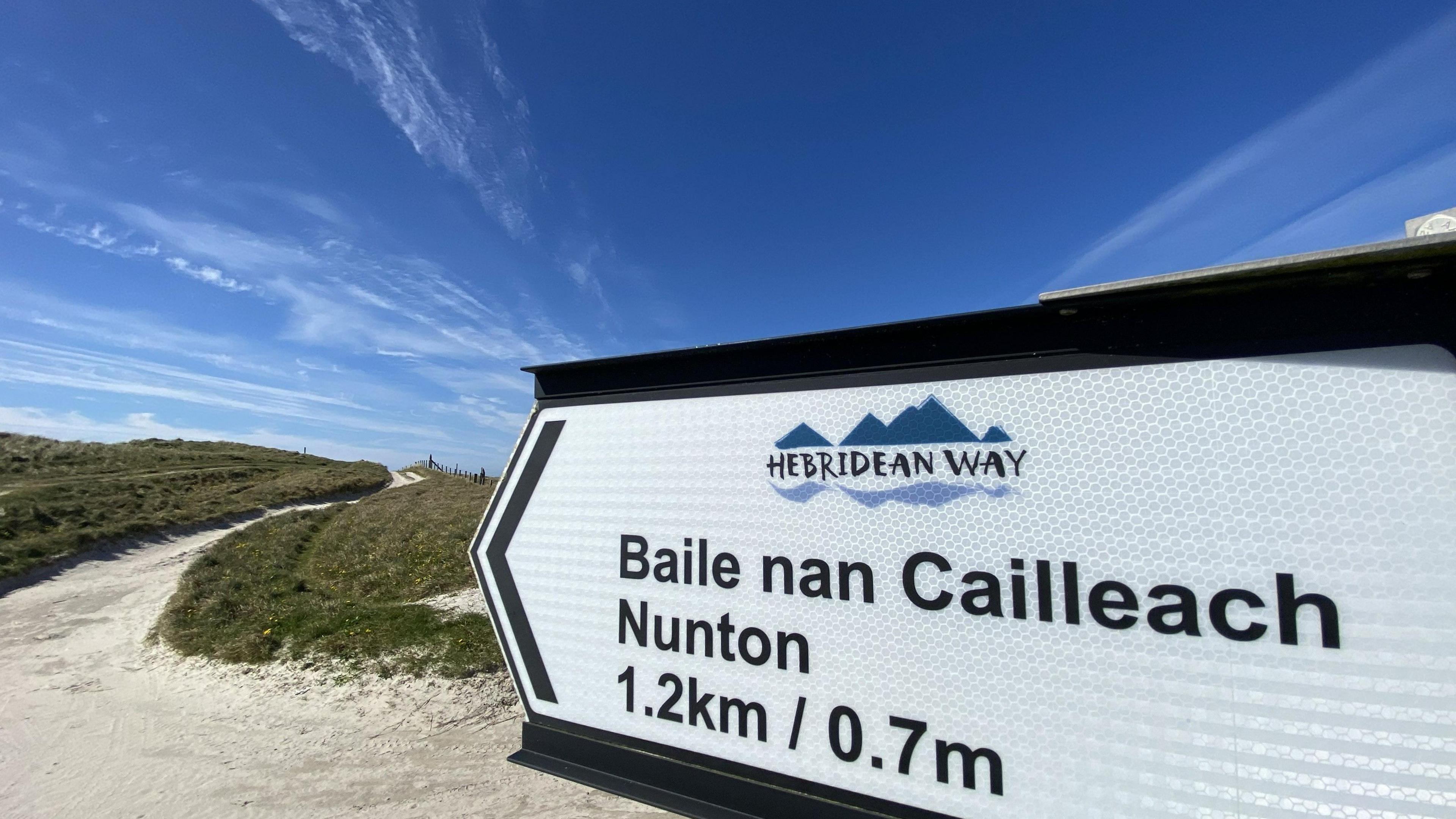 Soidhne air slighe Innse Gall aig tràigh air a bheil sgrìobhte Baile nan Cailleach, Nunton, agus an t-astar a tha ri dhol 