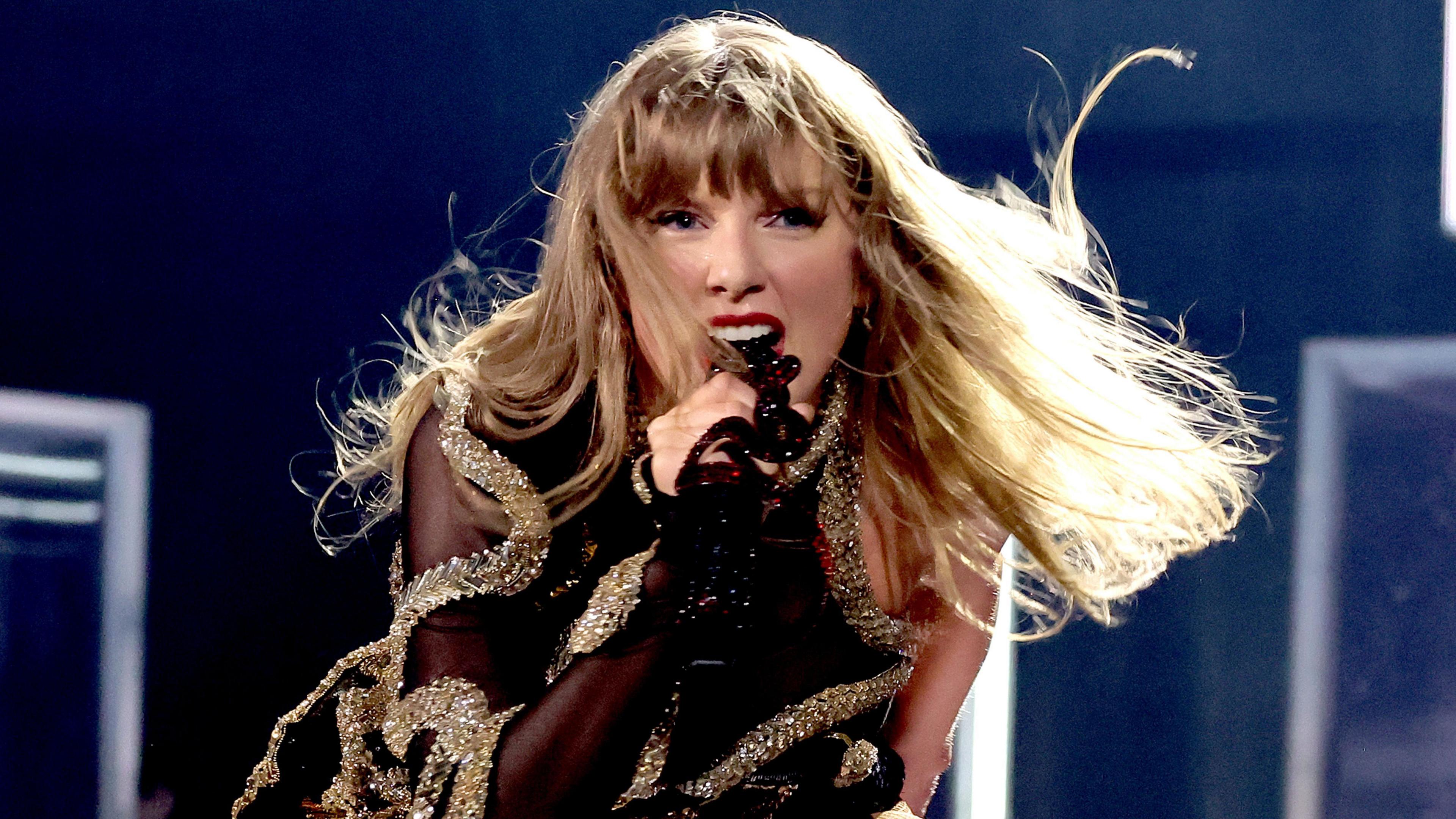 Taylor Swift on stage in Vancouver, wearing a black outfit braided with gold bands