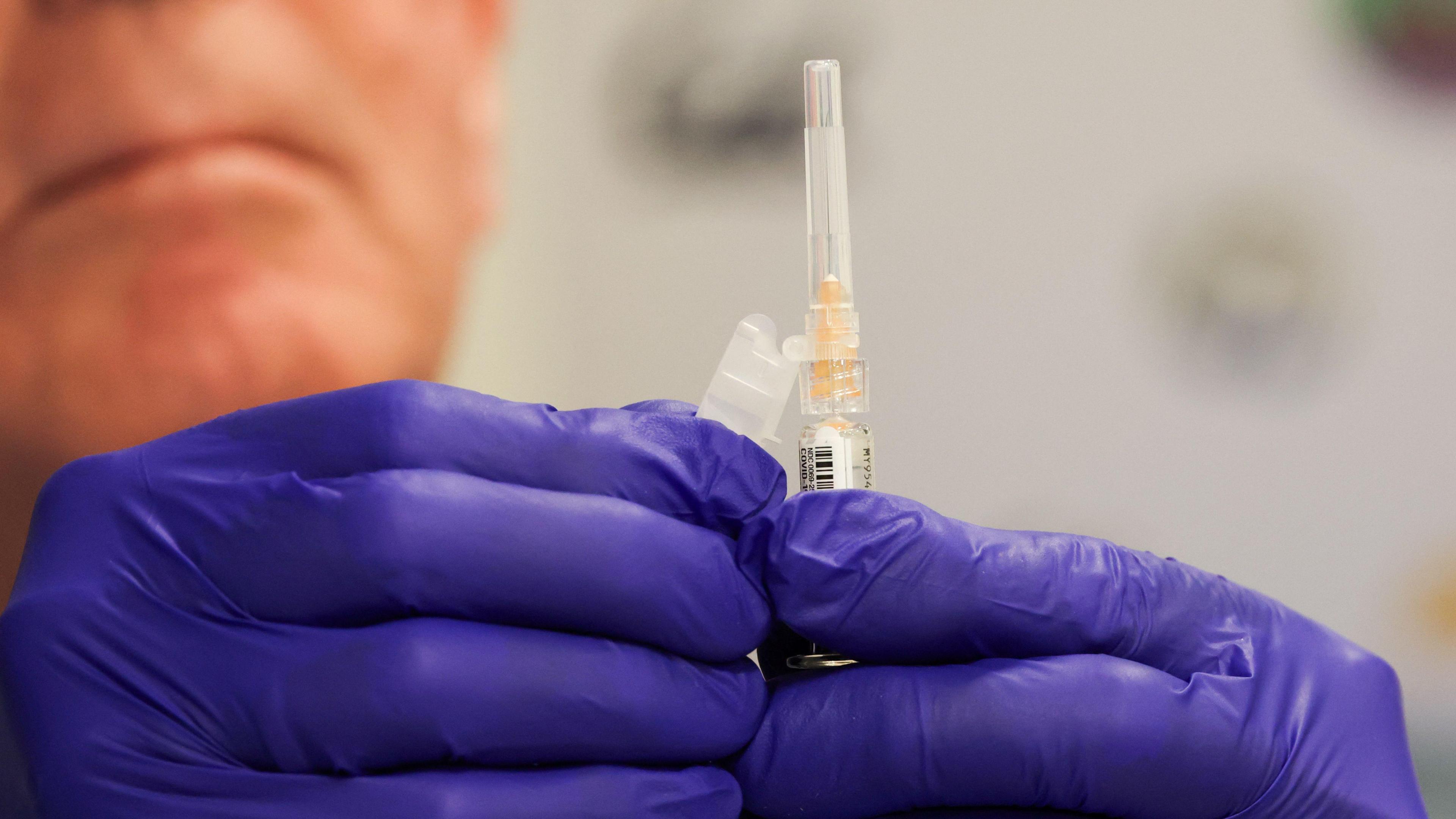 A pharmacist, who's wearing pruple gloves, prepares a vaccine shot.