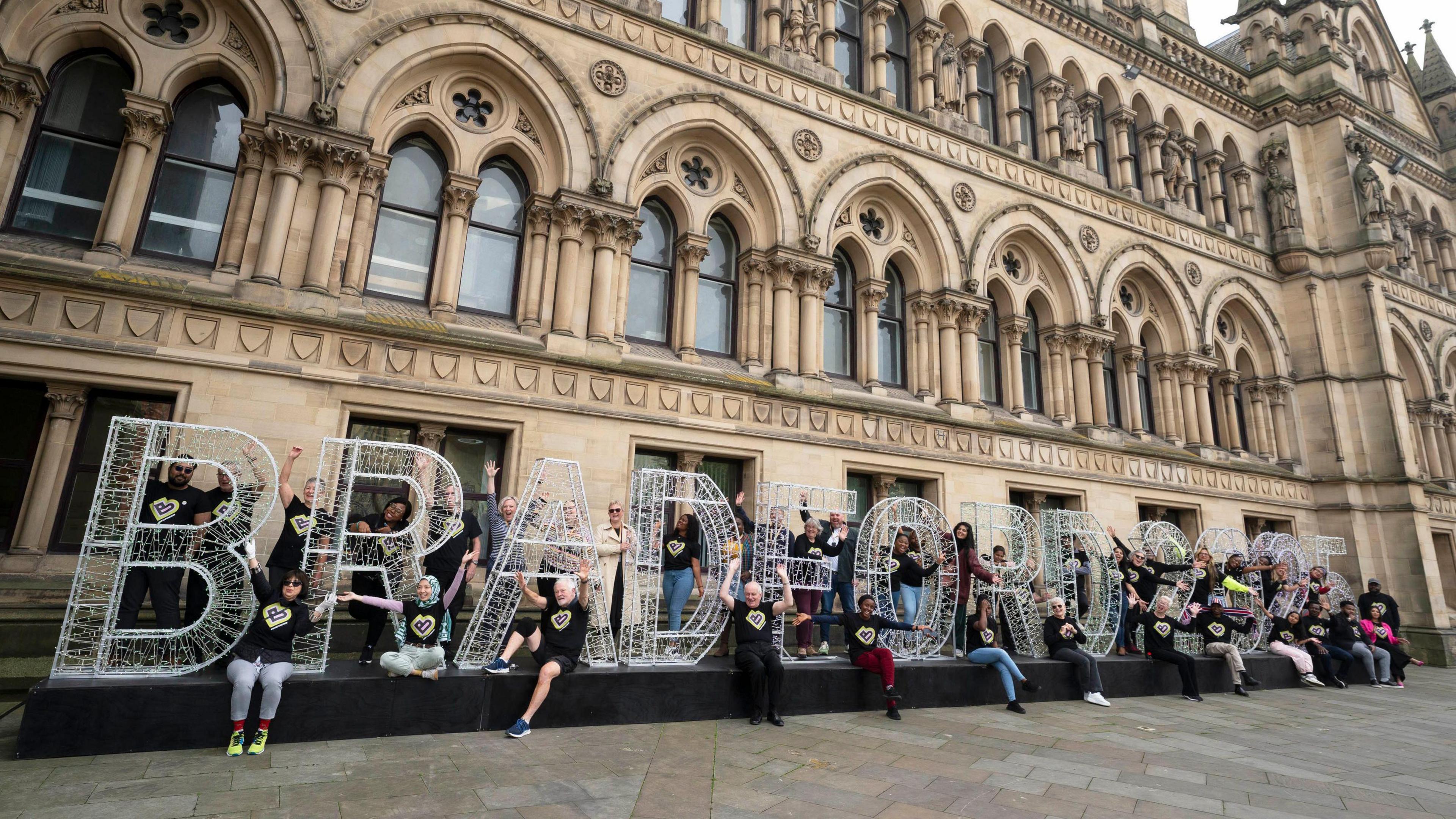 People in black t-shirts gather around a large display which spells out "Bradford 2025".