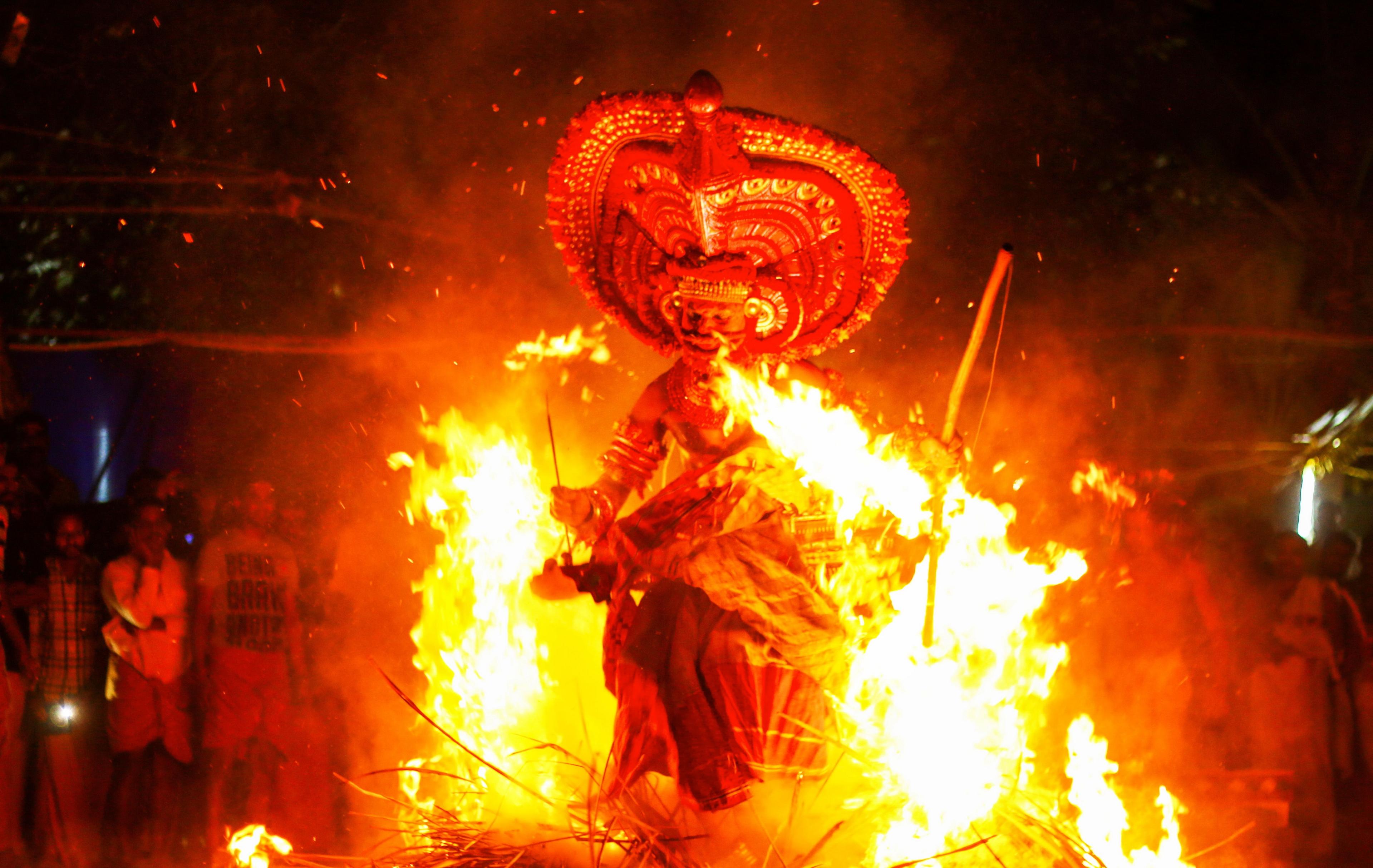 A man with a large headdress performing with fire, carrying burning torches