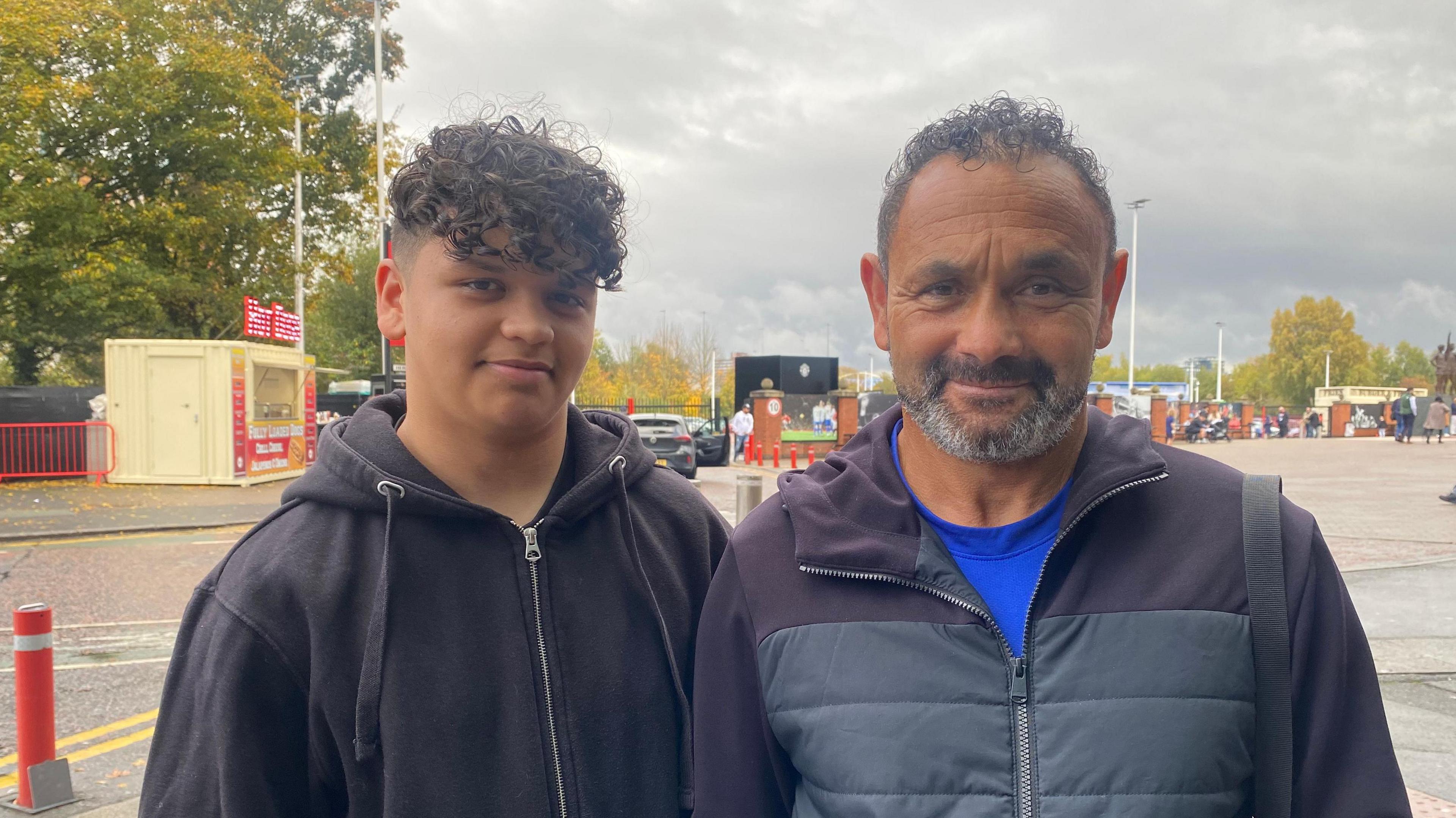 Ruben and Mark Stevenson, son and father, stand outside Old Trafford and smile for a photograph. 