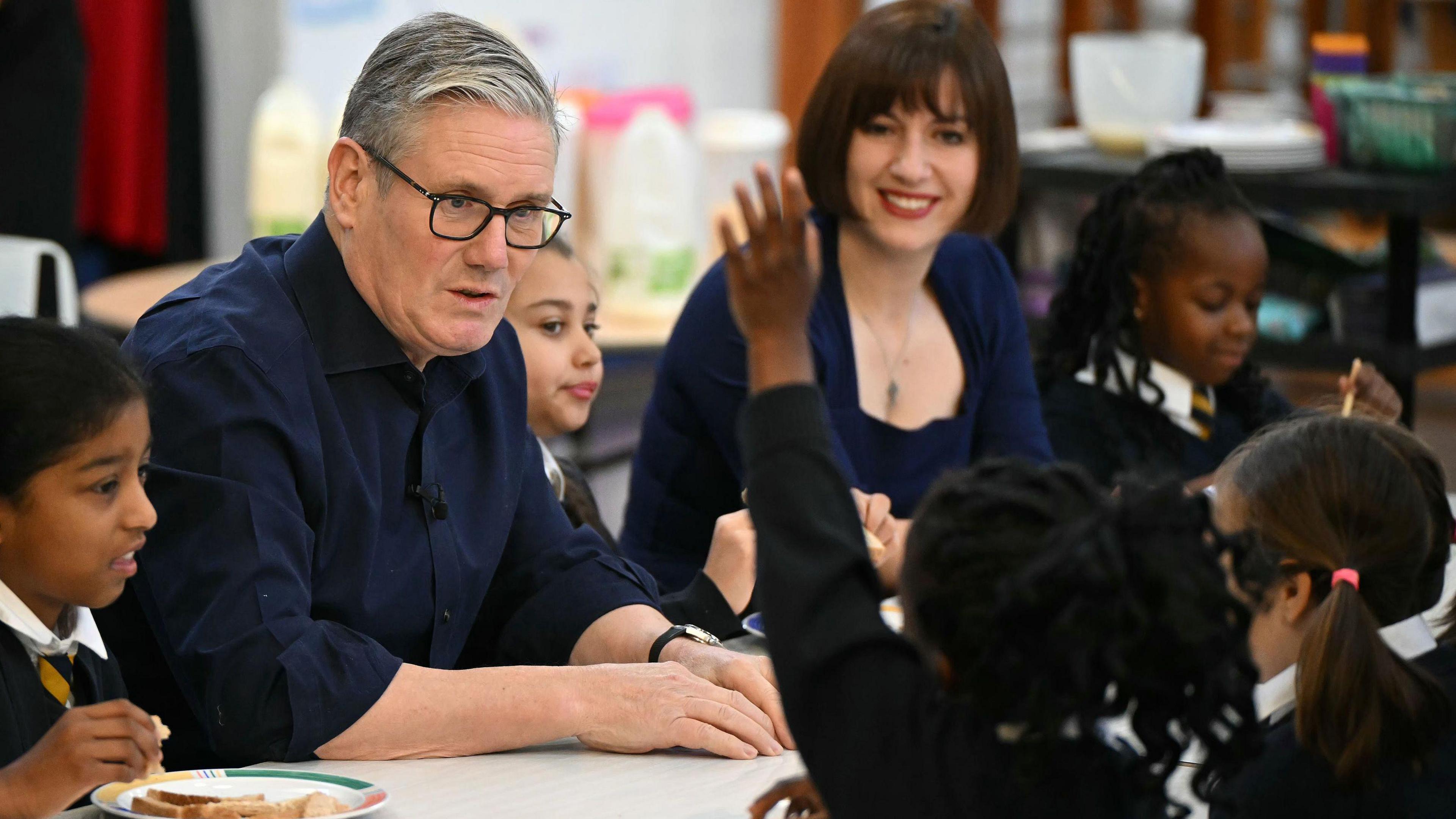 Prime Minister Sir Keir Starmer and Britain's Education Secretary Bridget Phillipson attend a breakfast club with students at St Anne's Catholic Primary School, near Reading, Berkshire, to announce the opening of applications for the national roll-out of free breakfast clubs. They are looking at one child who is raising her hand.