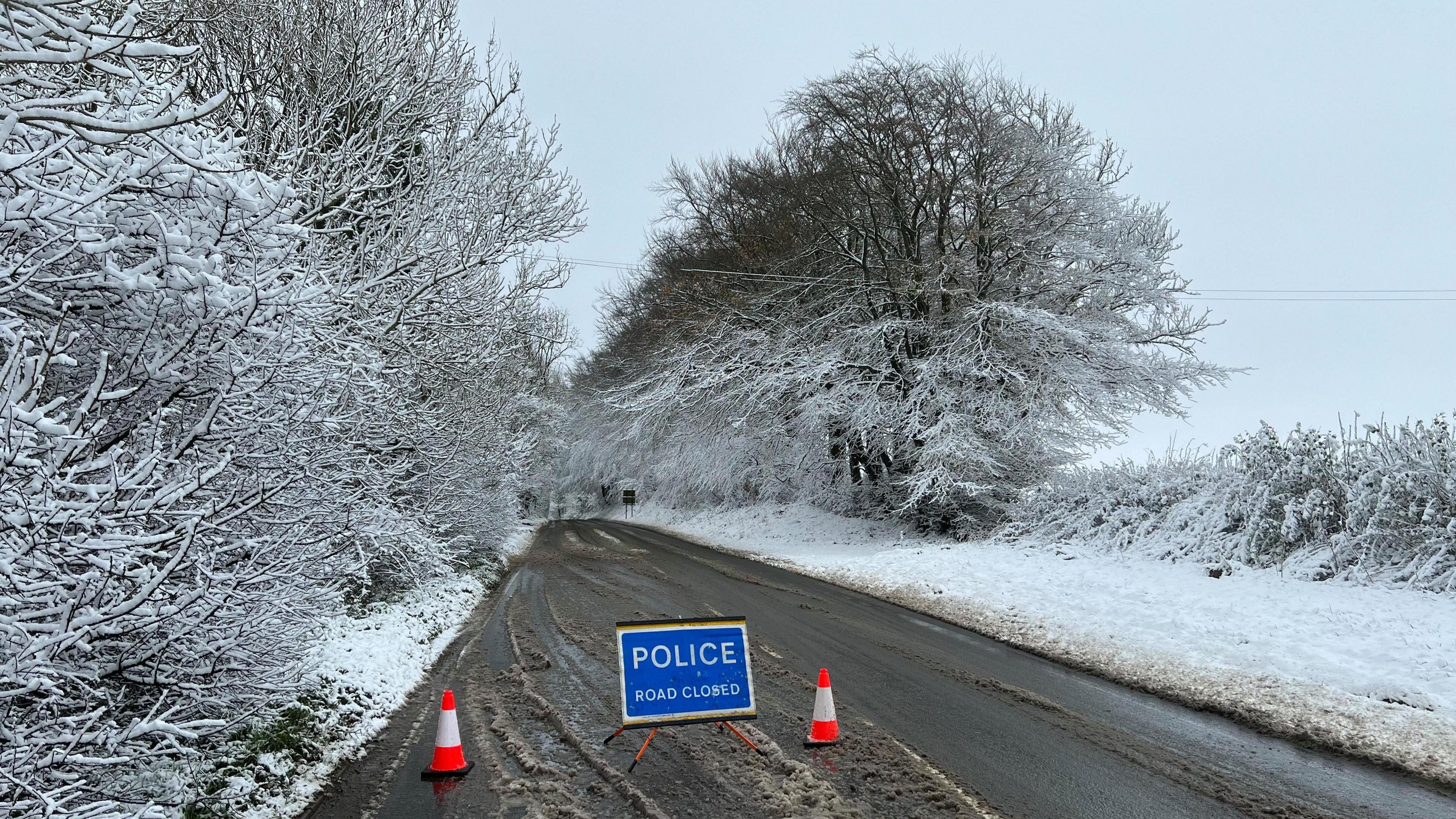 A snowy road with a 'Police: Road closed' sign