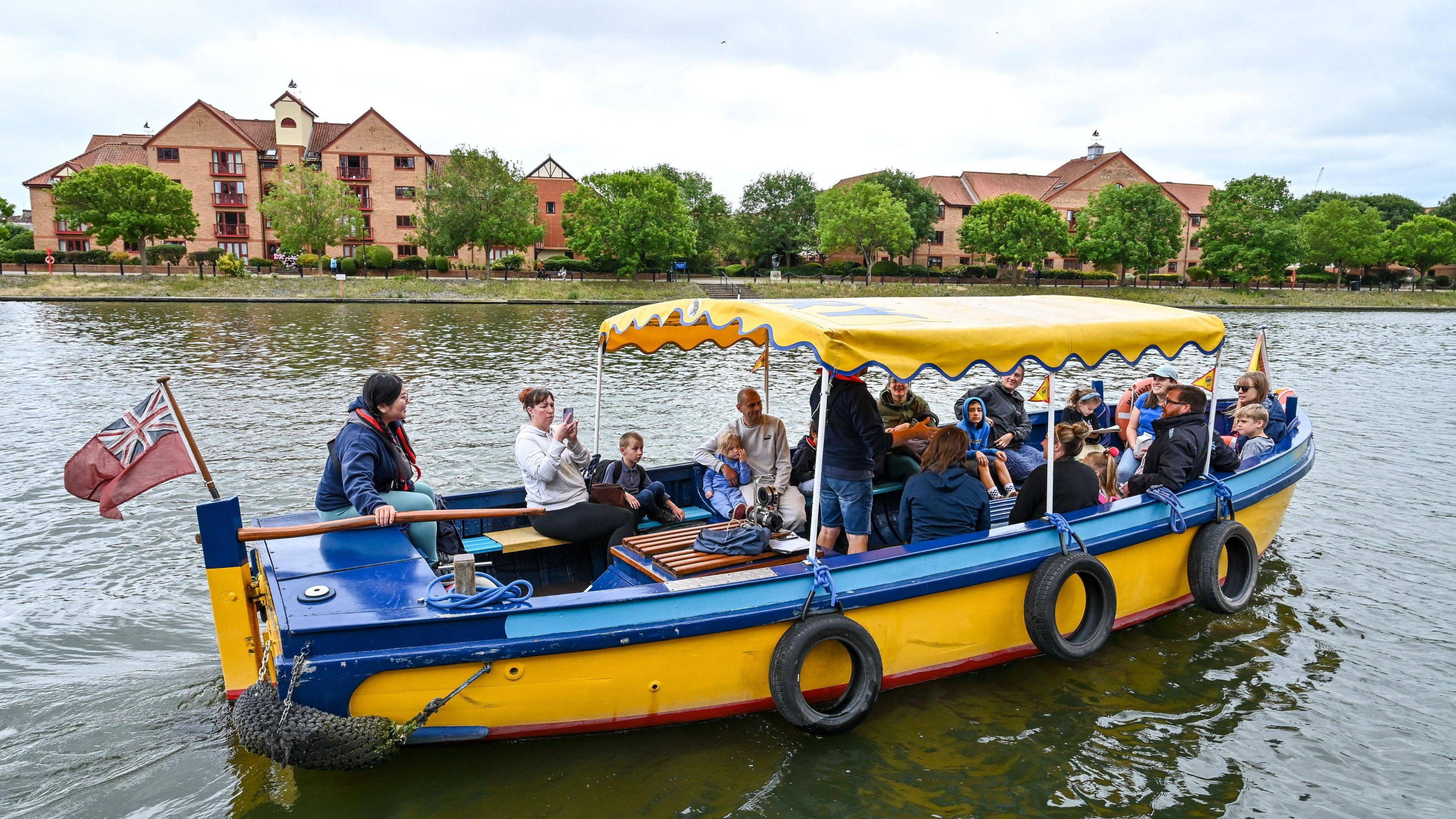 A yellow and blue ferry carrying children and adults near Bristol harbour