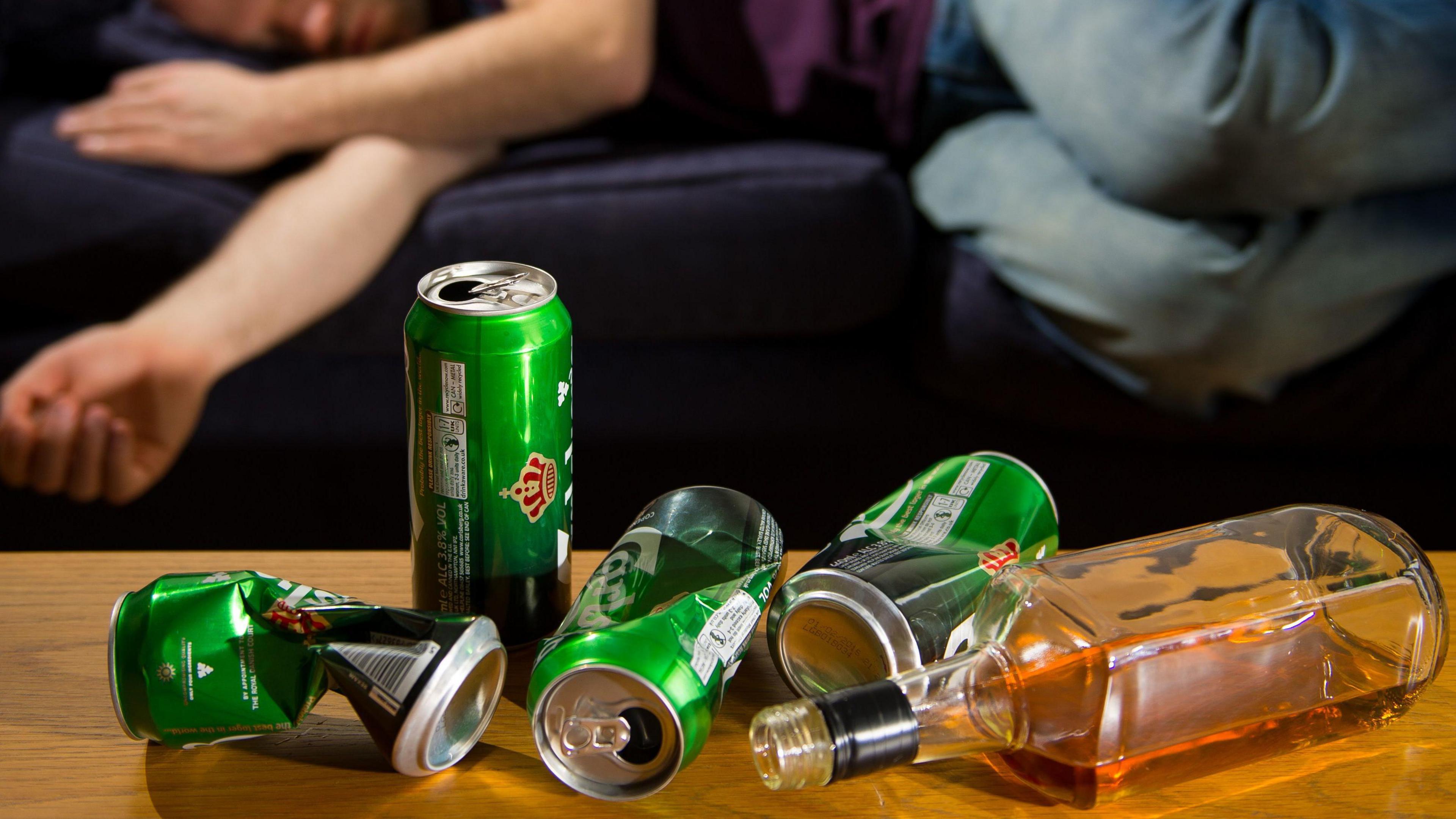 Man lying down with crushed and empty beer cans in front of him 