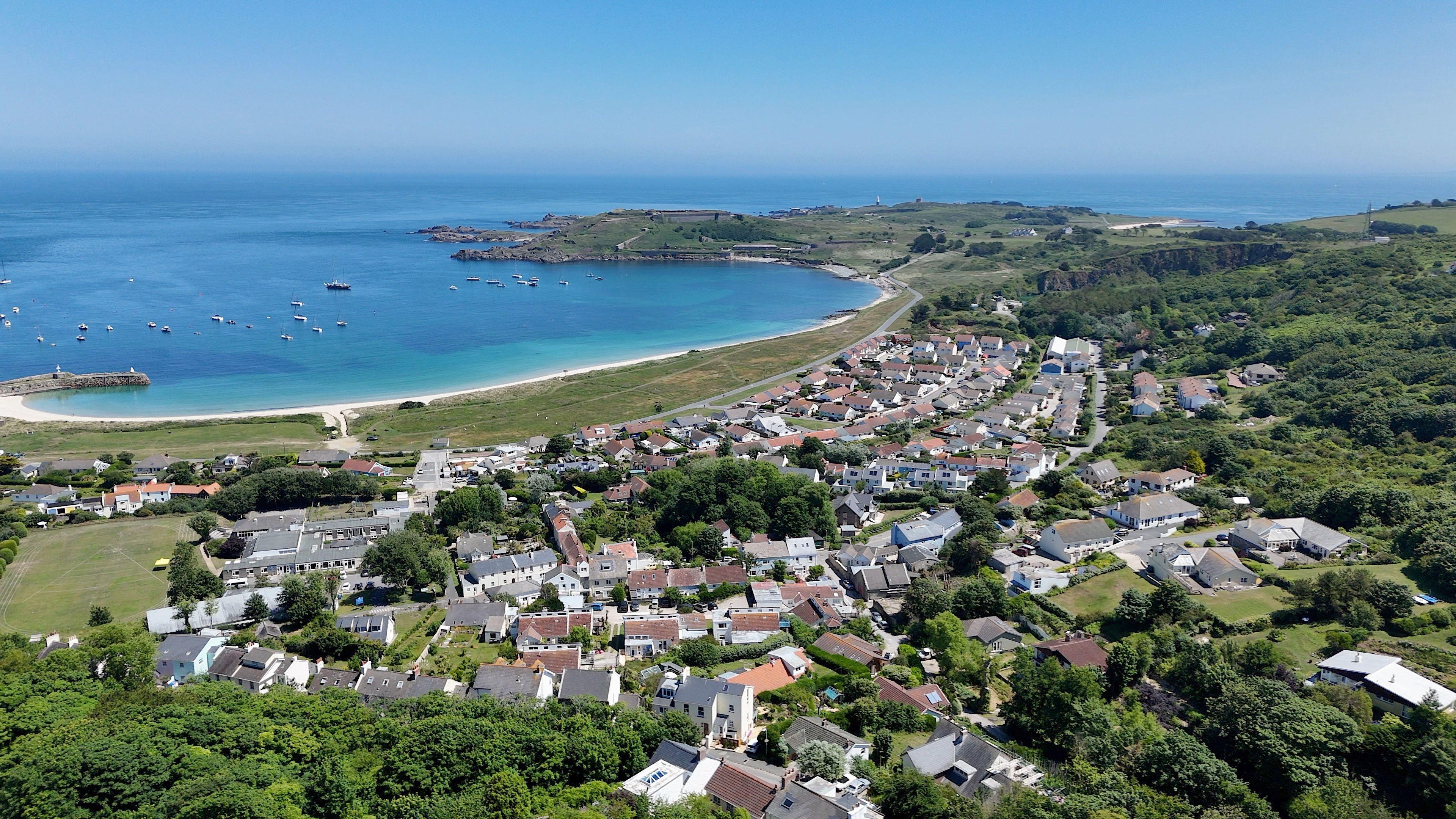 An aerial view over a small town on an island, with a sweeping sandy bay behind.
