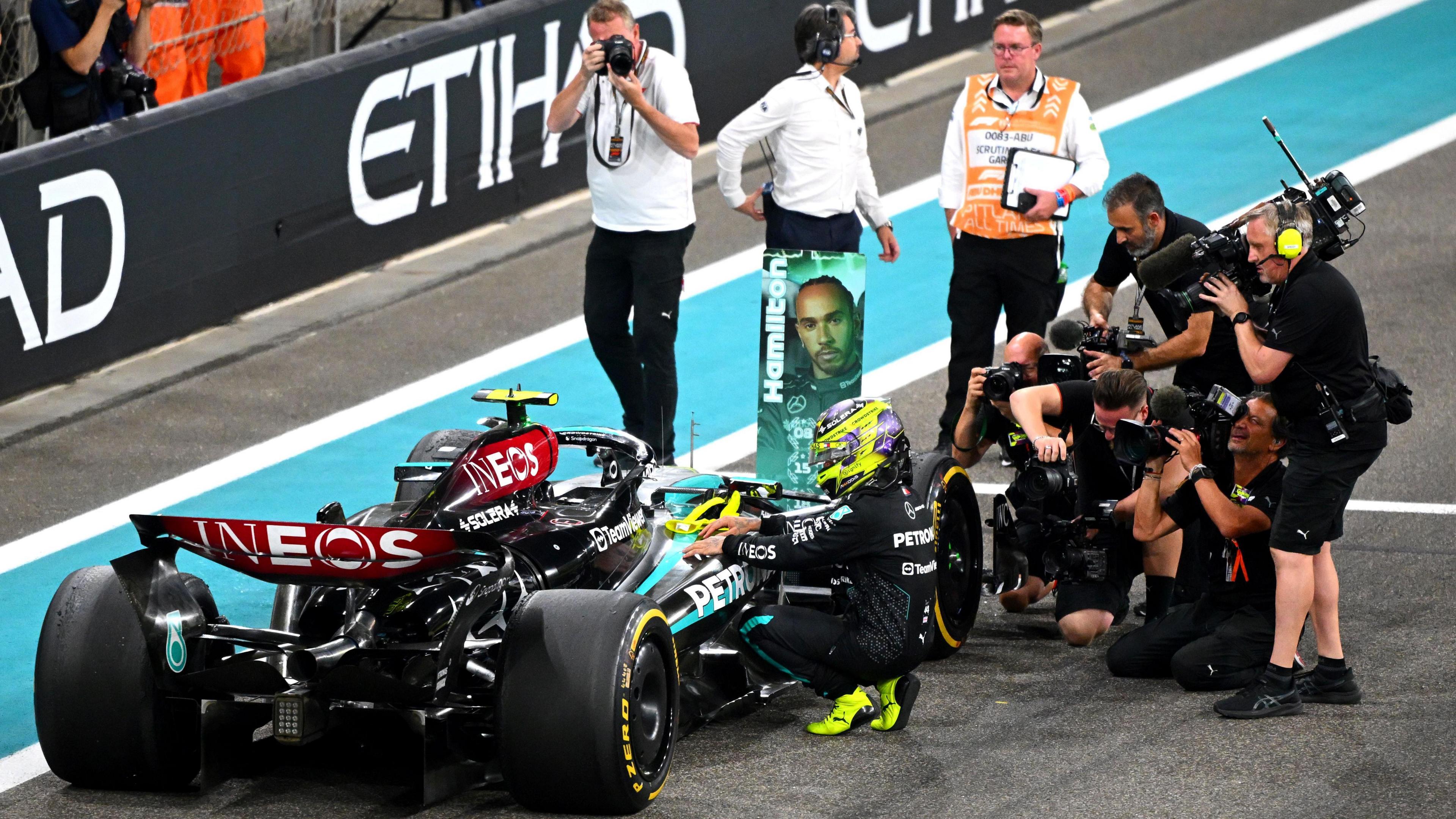 Lewis Hamilton is photographed kneeling against his car after finishing his last race with Mercedes in Abu Dhabi