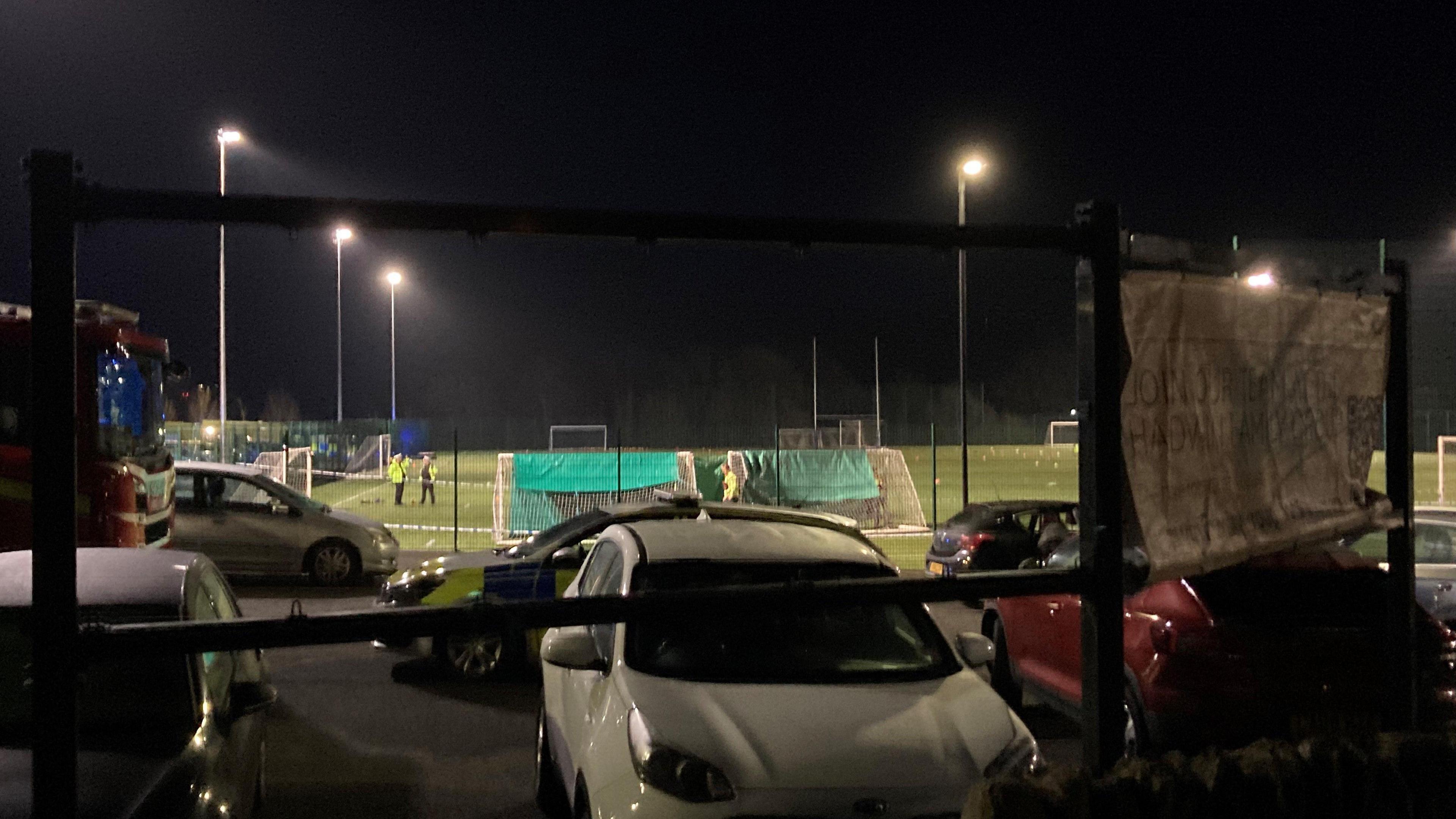 A zoomed out view of the scene. Police tape can be seen on the pitch with police officers standing next to the goals.