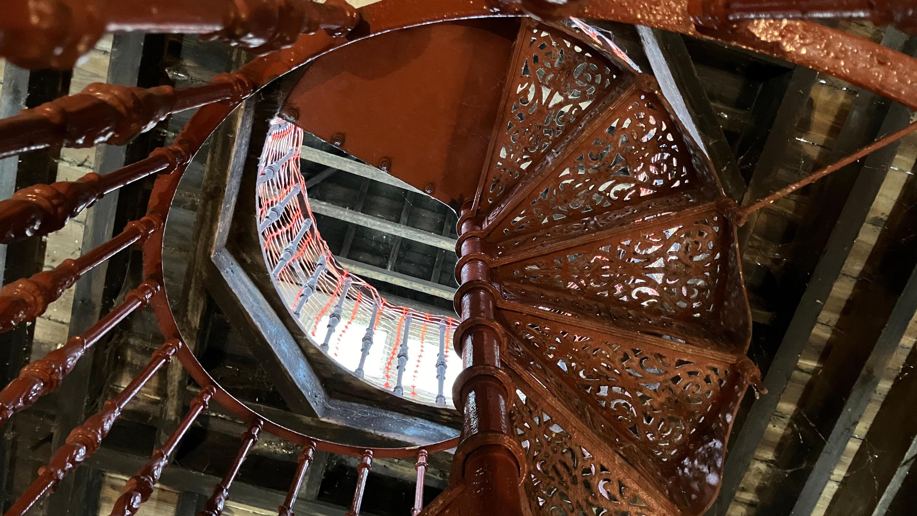 A spiral staircase made of intricate cast iron patterns leads to a loft space filled with light