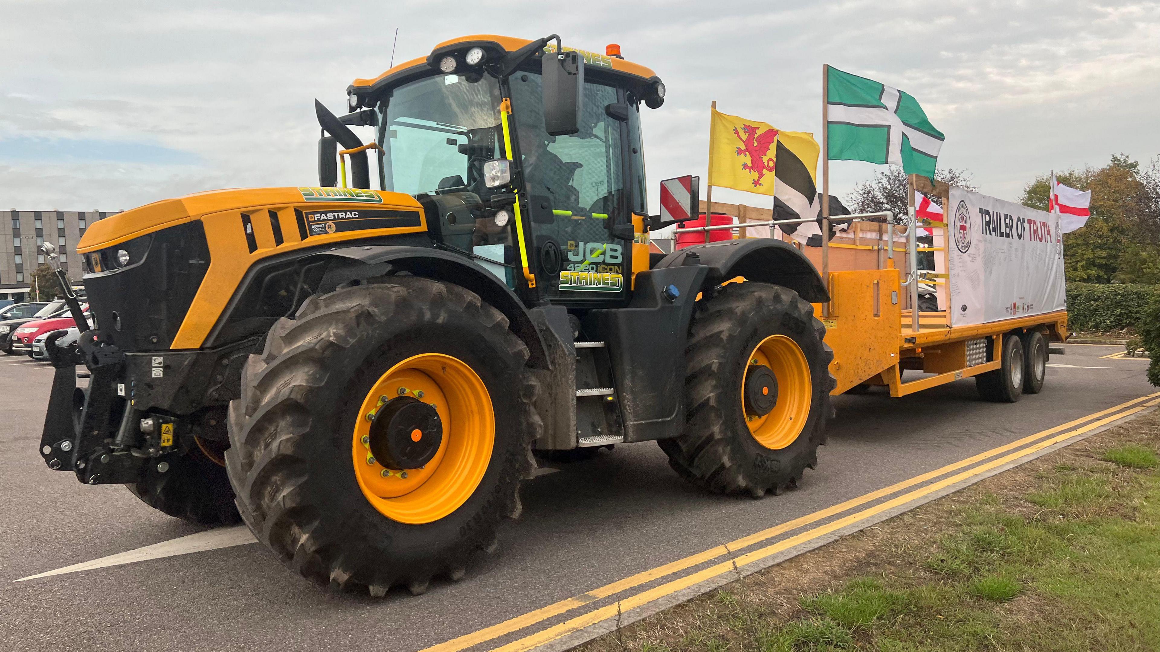 A yellow tractor with a trailer attached to the back. There are several flags attached to the back of the trailer.