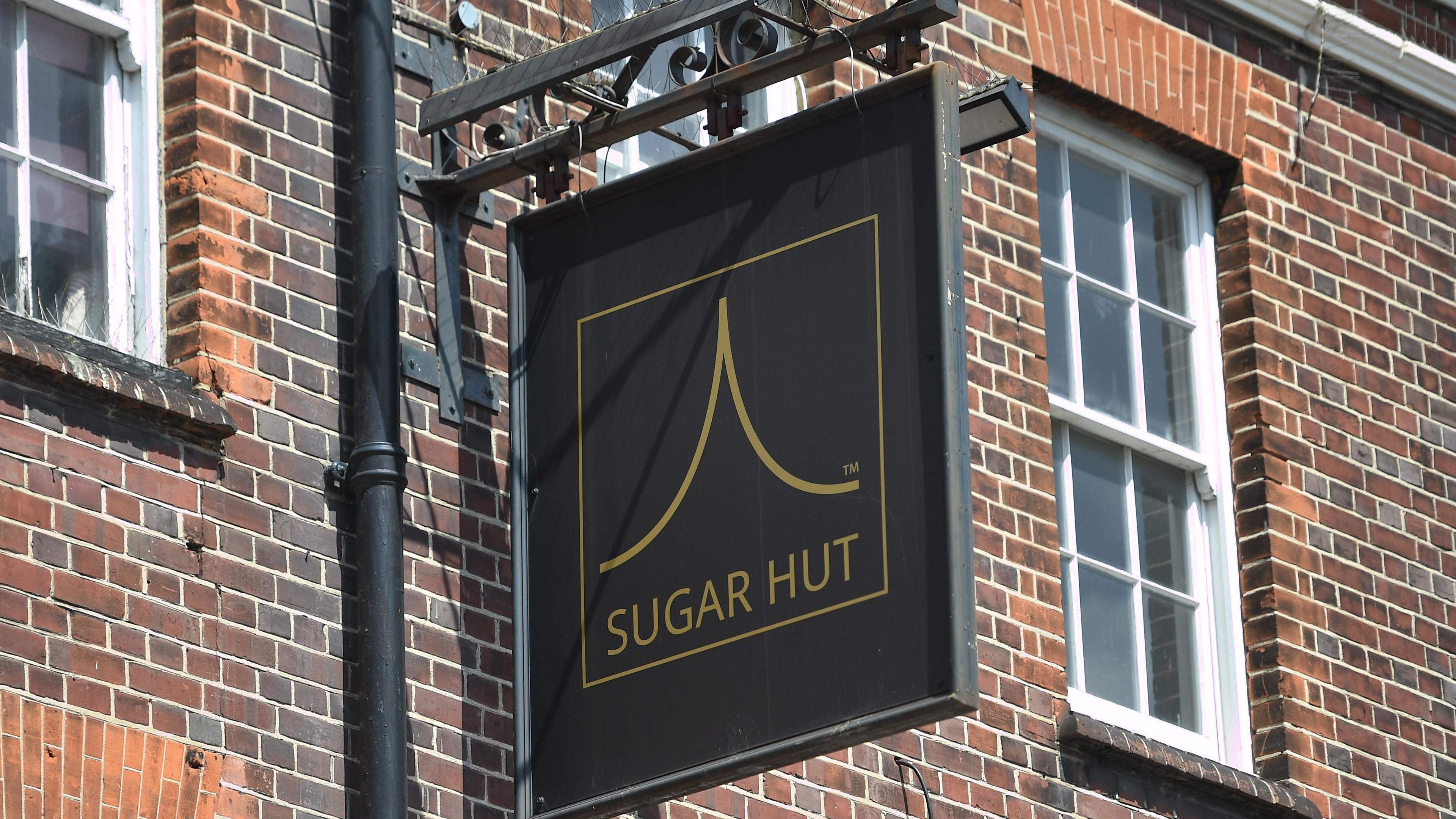 Black sign with gold text reading sugar hut undernath the Sugar Hut logo.